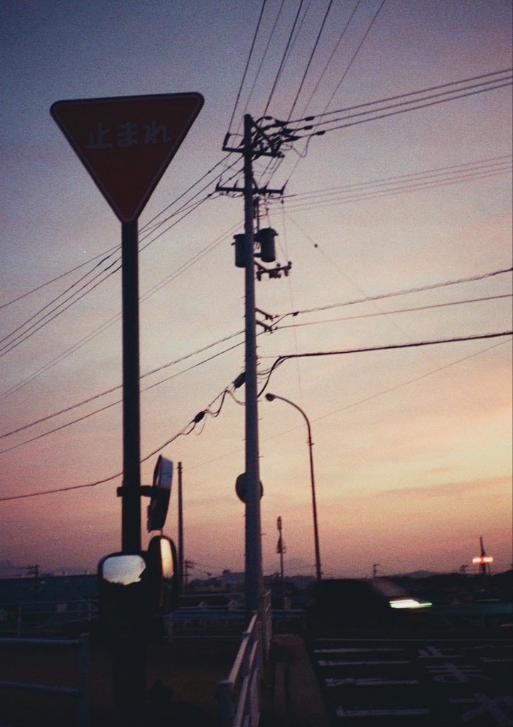夕焼け空の下、電線と街灯が並ぶ交差点の風景