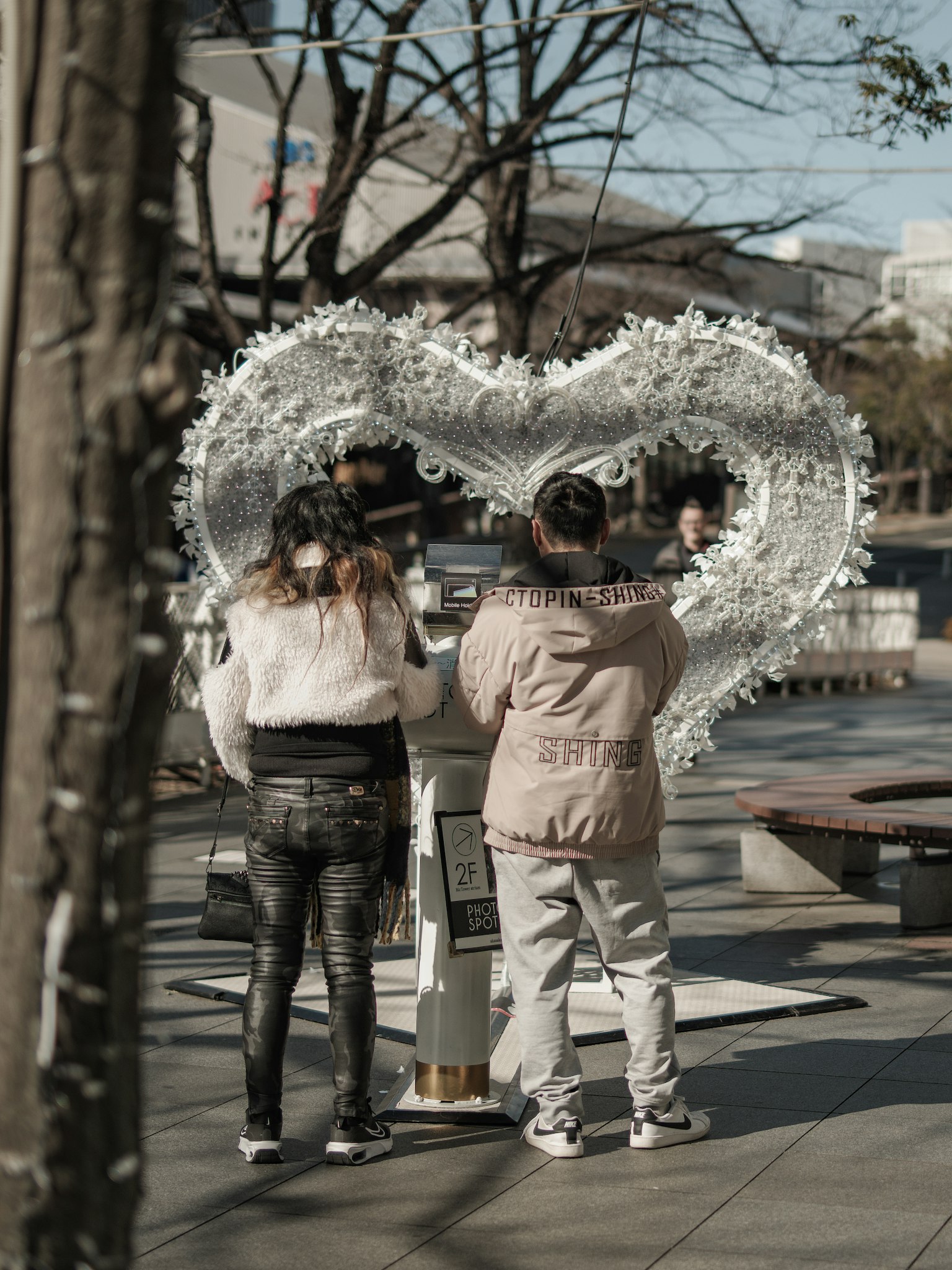 공원에서 큰 흰색 하트 모양의 조형물 앞에 서 있는 두 사람
