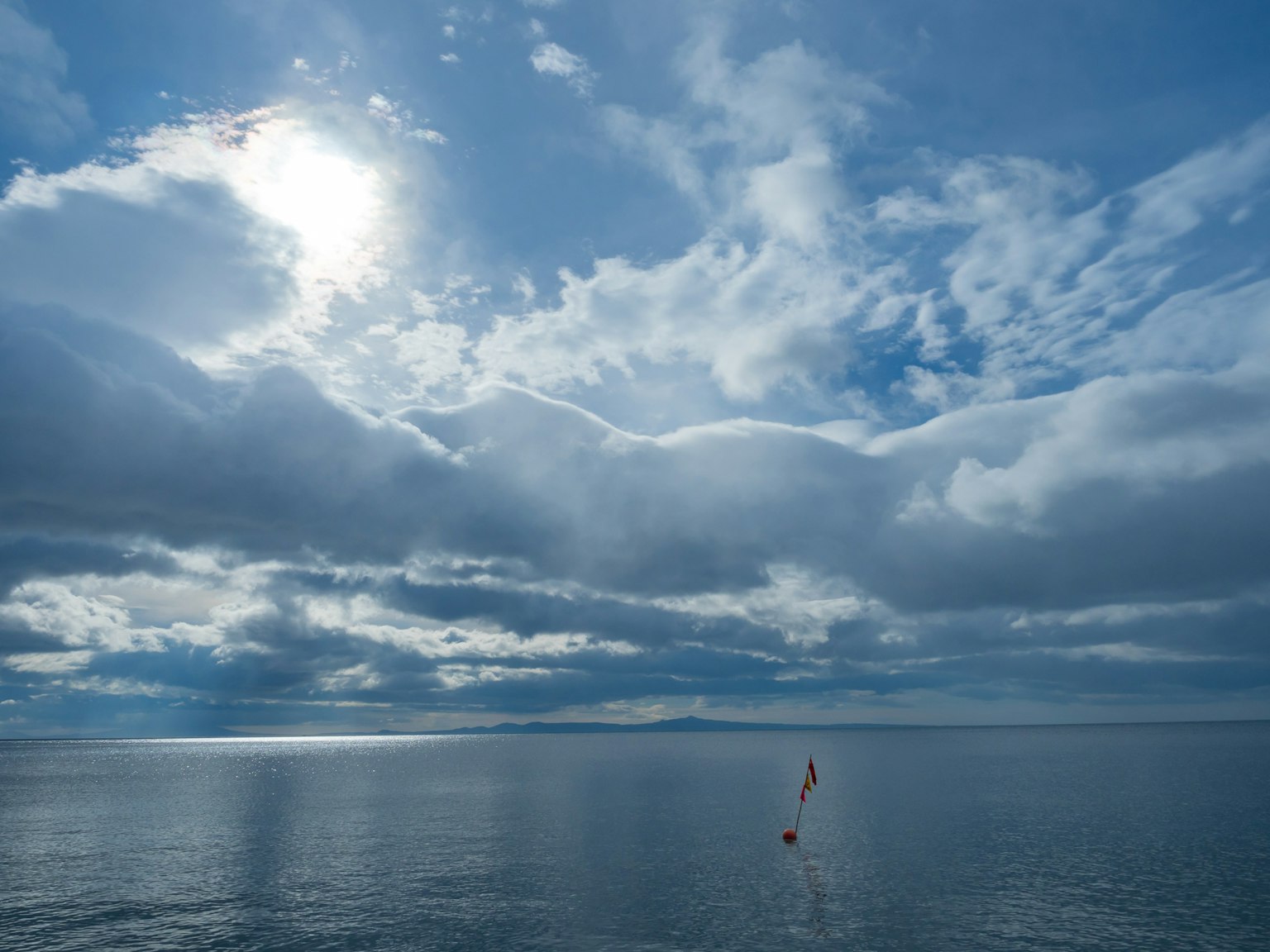 Una piccola barca a vela su un mare calmo sotto un cielo blu con nuvole