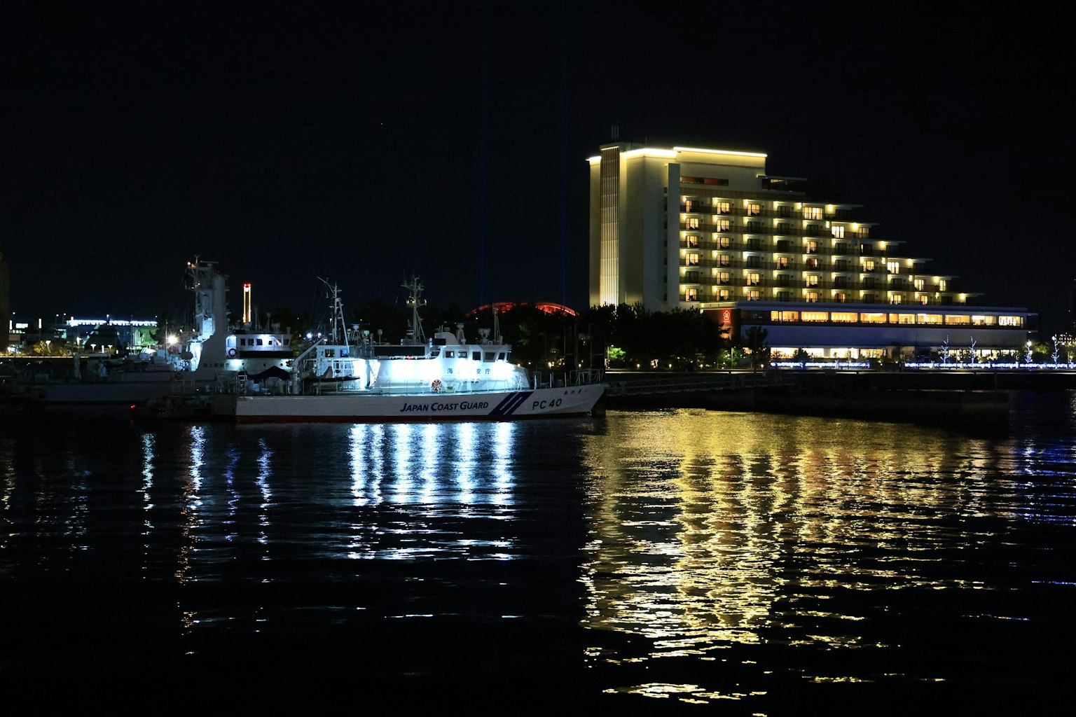 Hermosa vista nocturna de un puerto con barcos iluminados y un hotel