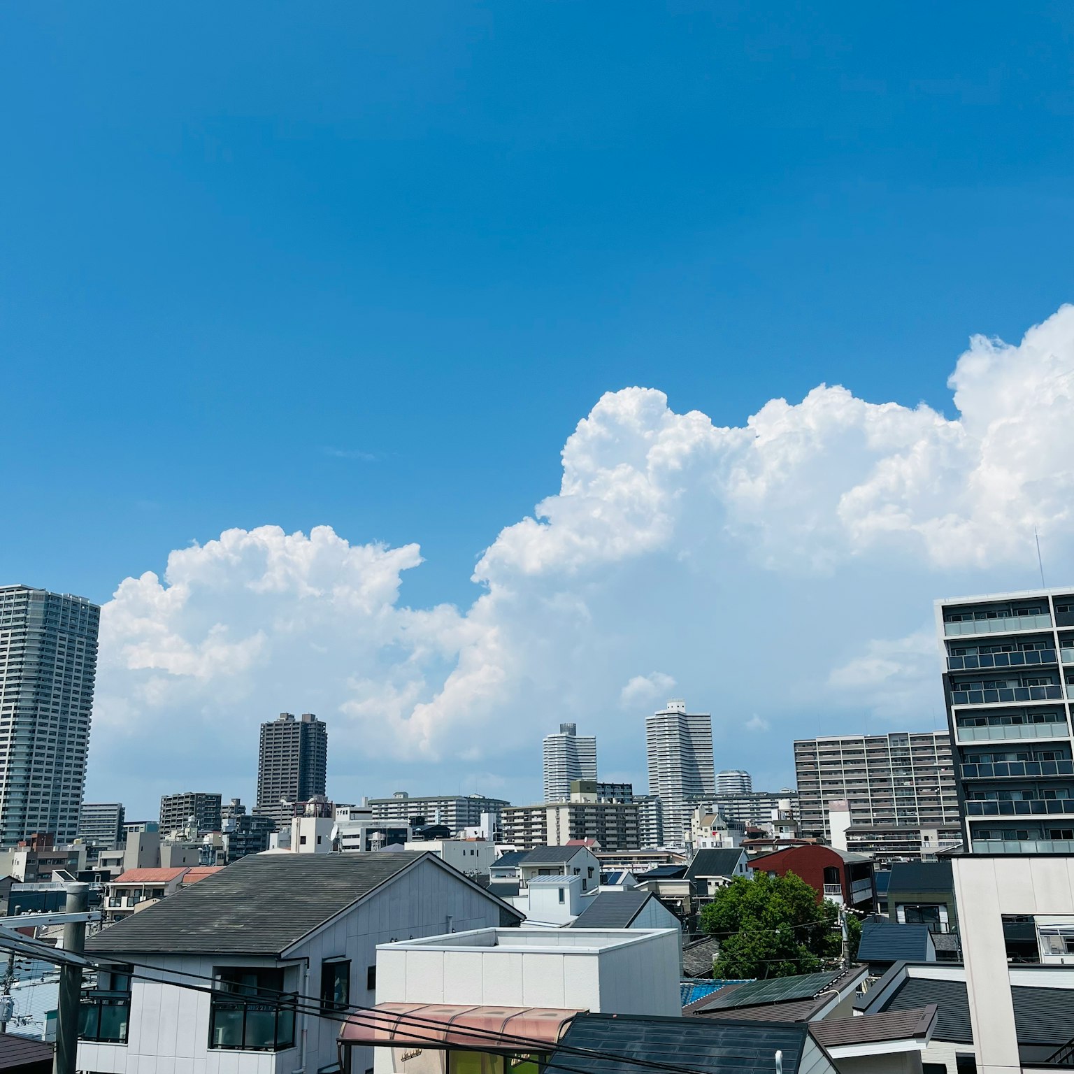 Urban skyline featuring tall buildings and residential areas under a clear blue sky with fluffy white clouds