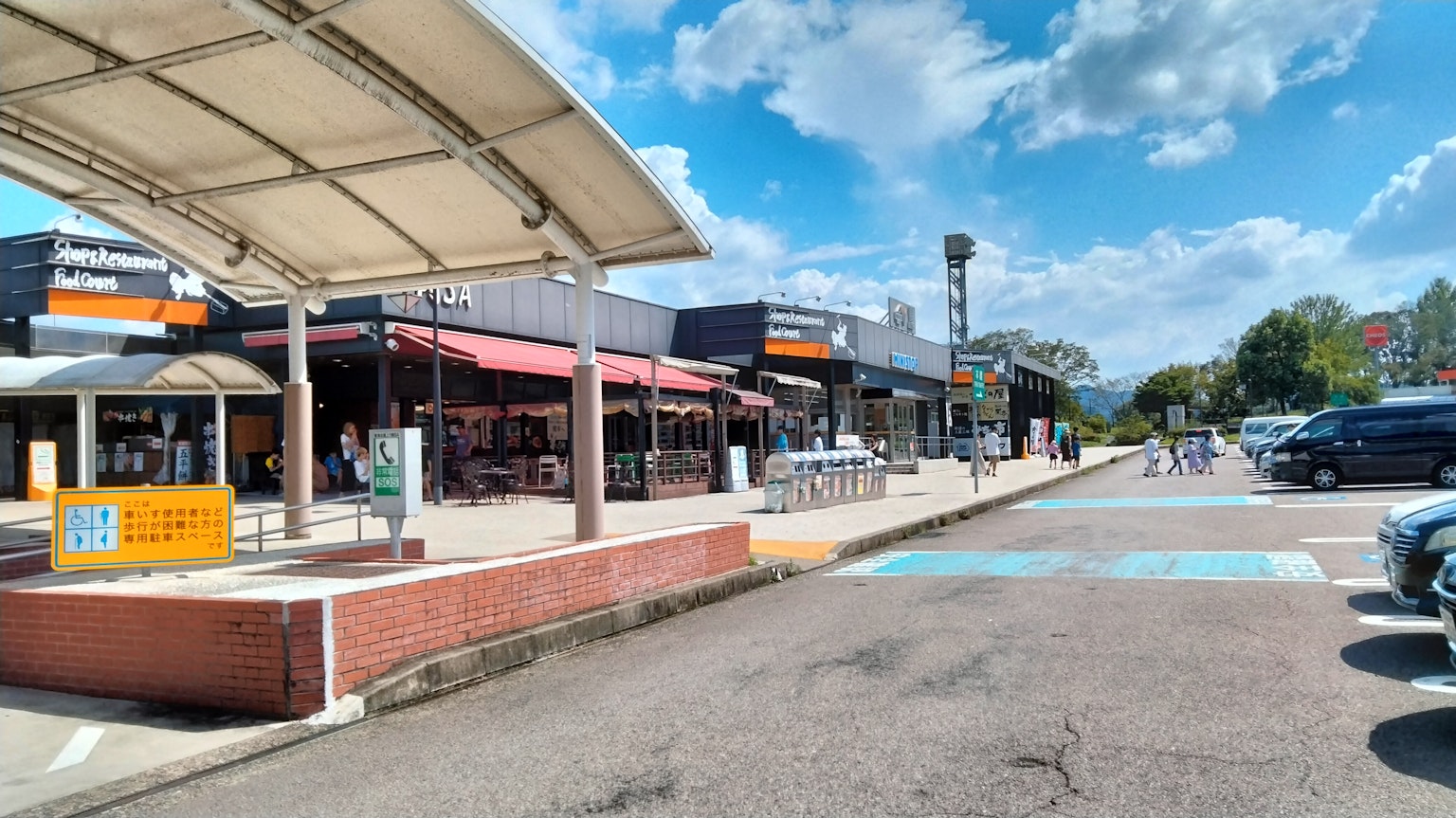 Zona comercial al aire libre con cafeterías y tiendas bajo un cielo azul con nubes