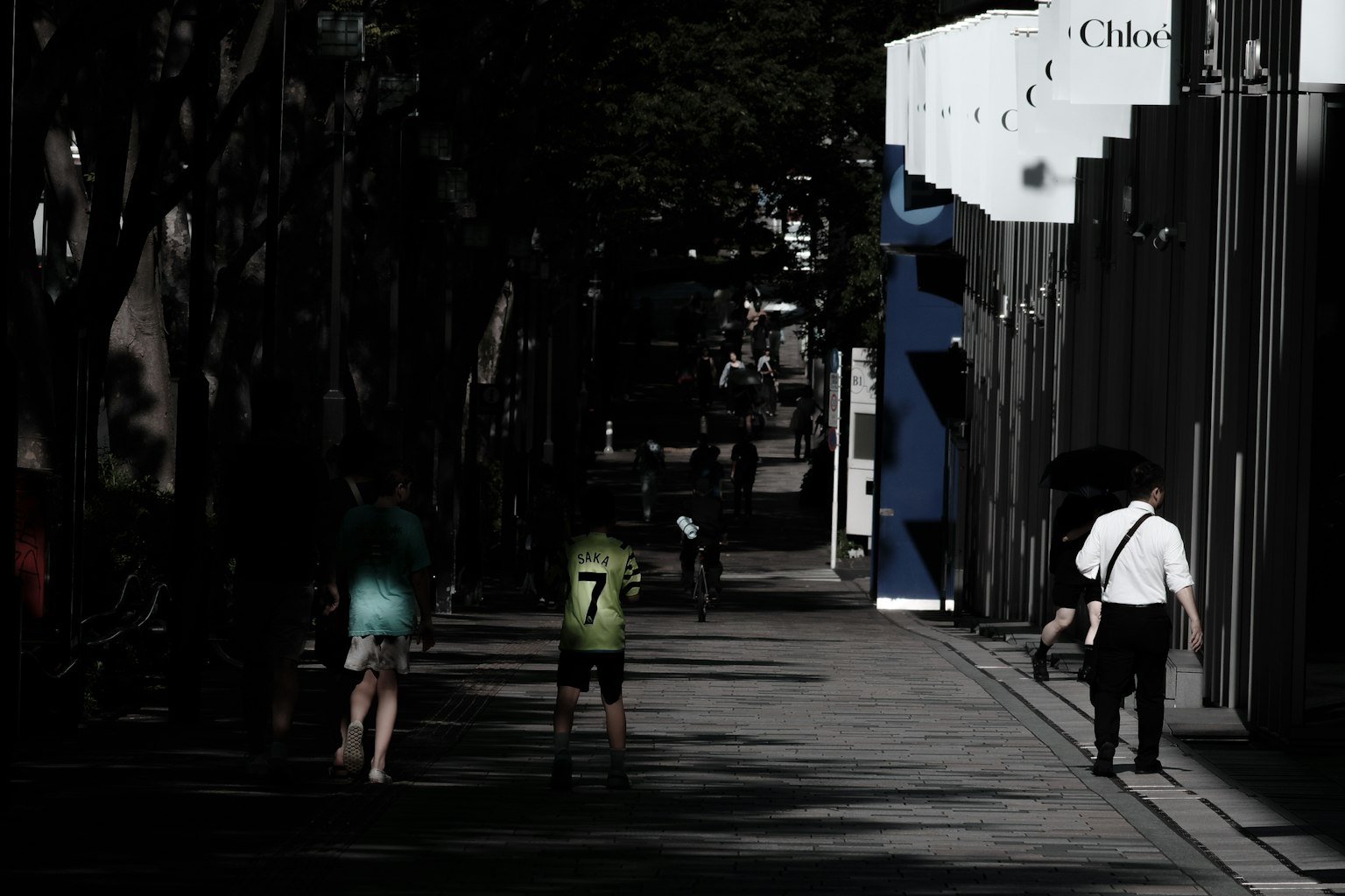 People walking in a dimly lit street with building shadows