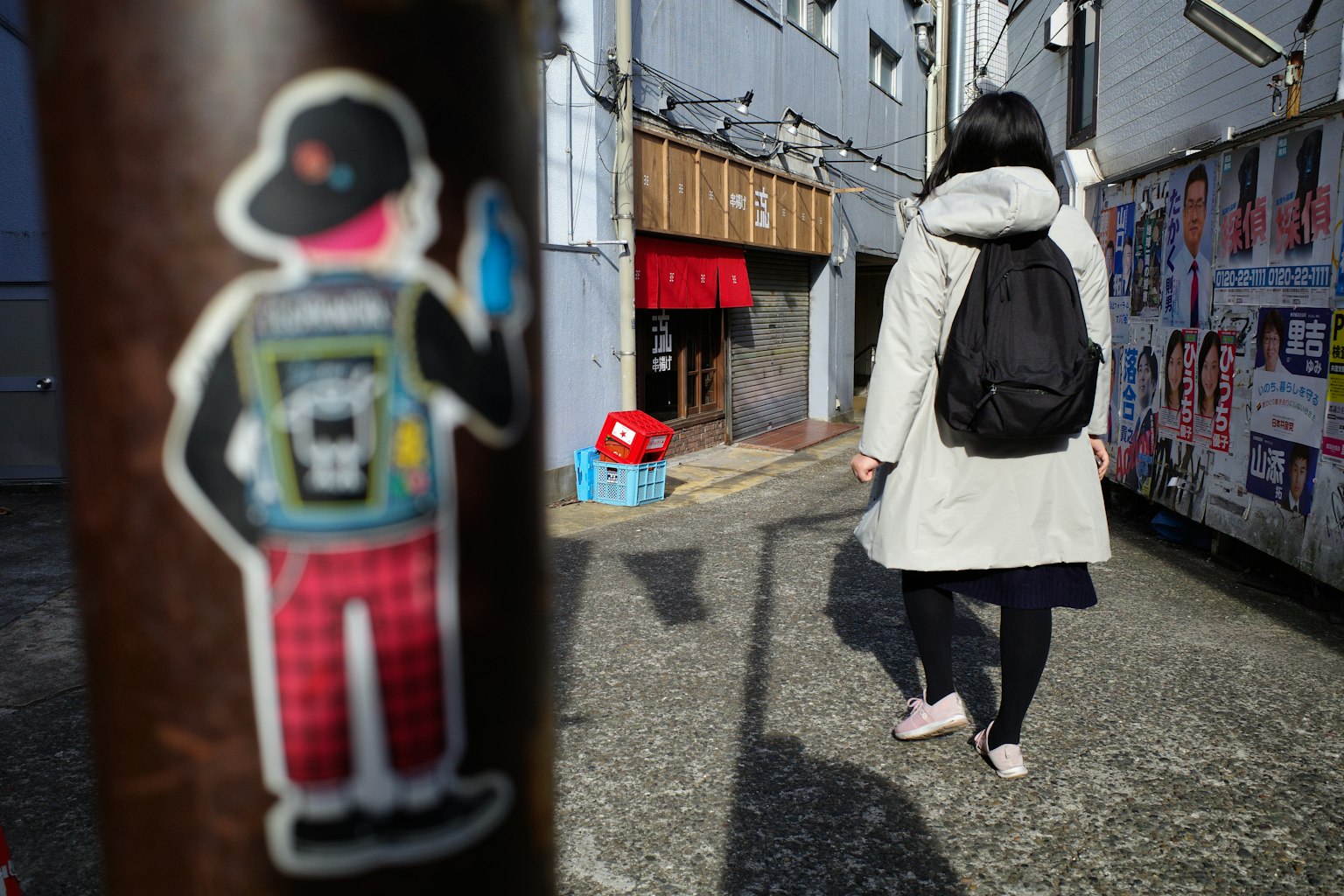 Une femme marchant avec un sac à dos dans un environnement urbain avec un autocollant de personnage sur un poteau