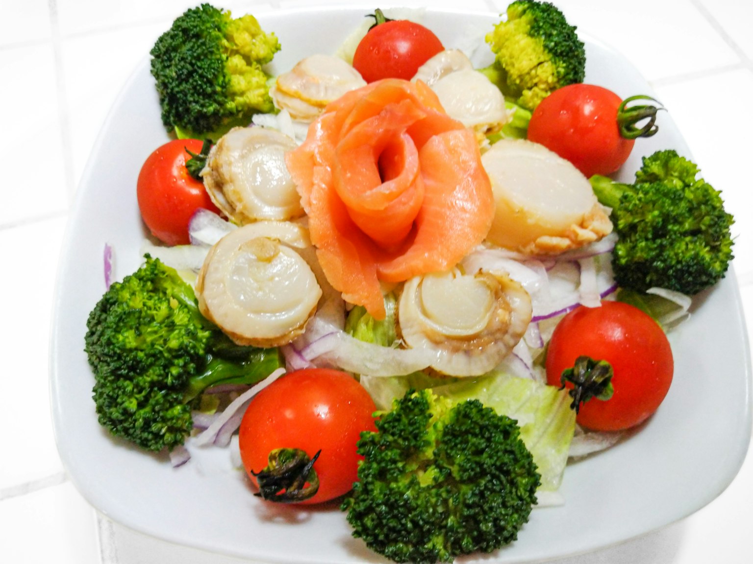 A vibrant salad plate featuring tomatoes and broccoli surrounding a rose made of smoked salmon