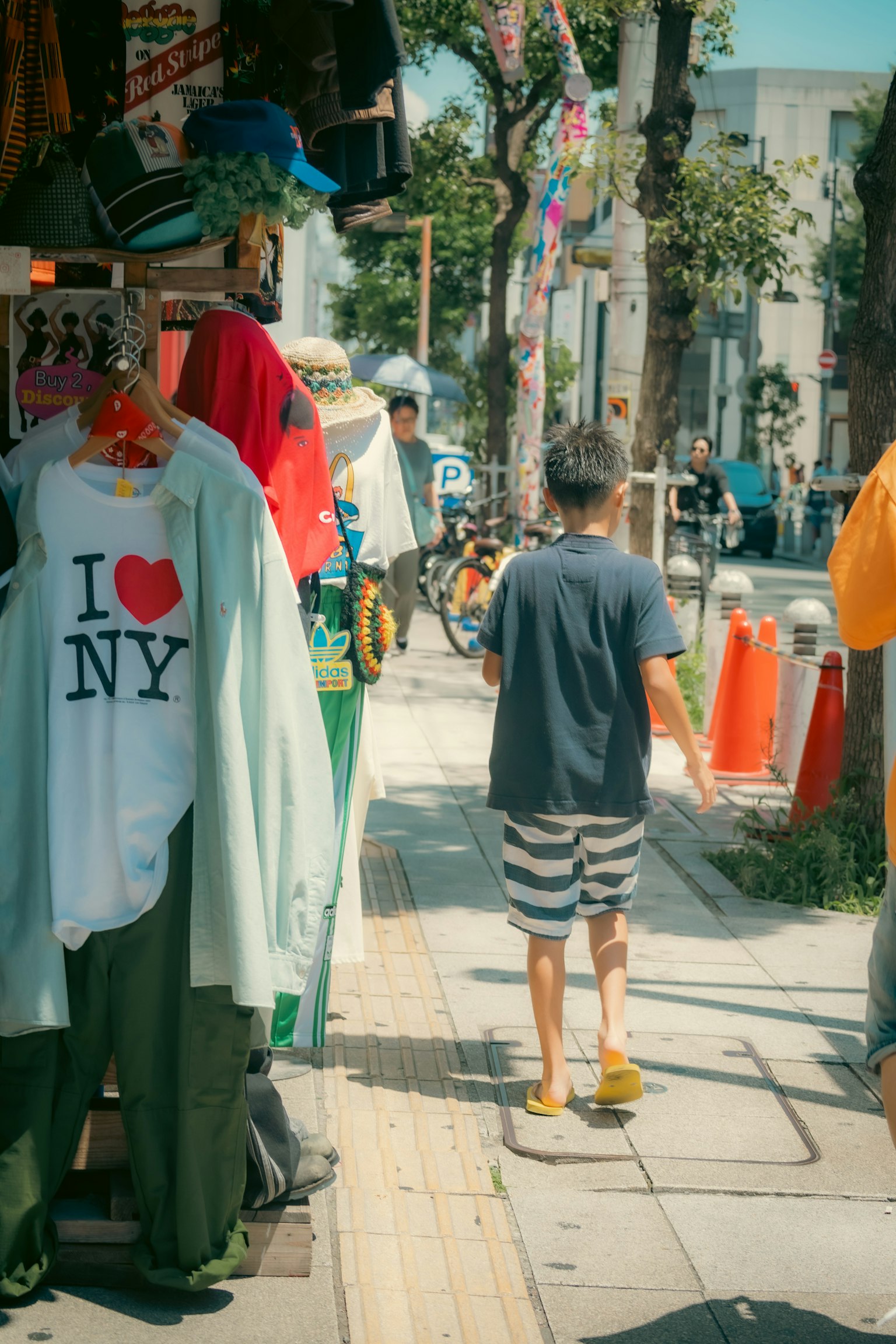 เด็กชายเดินผ่านร้านเสื้อผ้าบนถนนที่มีเสื้อผ้าหลากสี