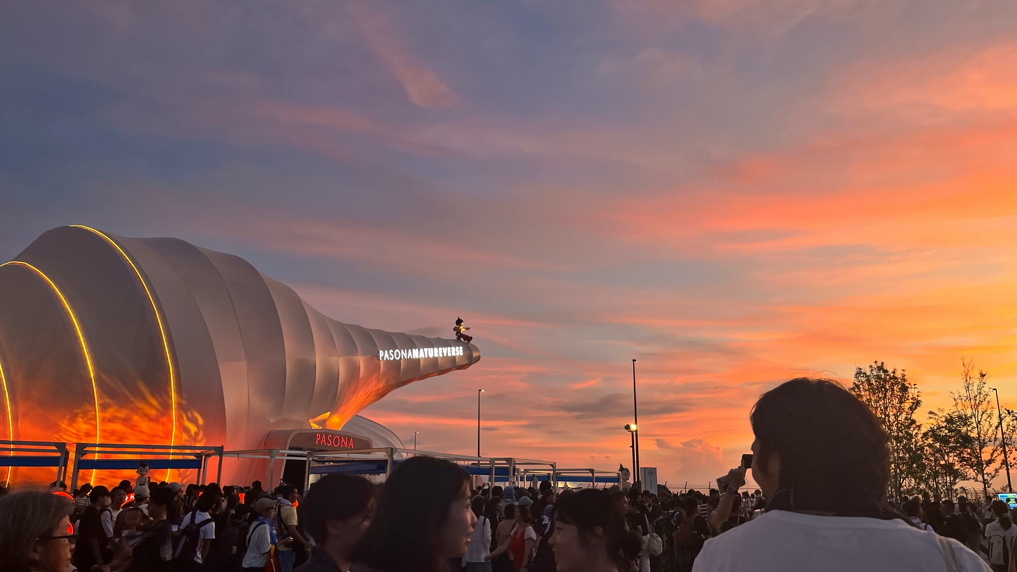 夕焼けの下で人々が集まるスタジアム前の広場