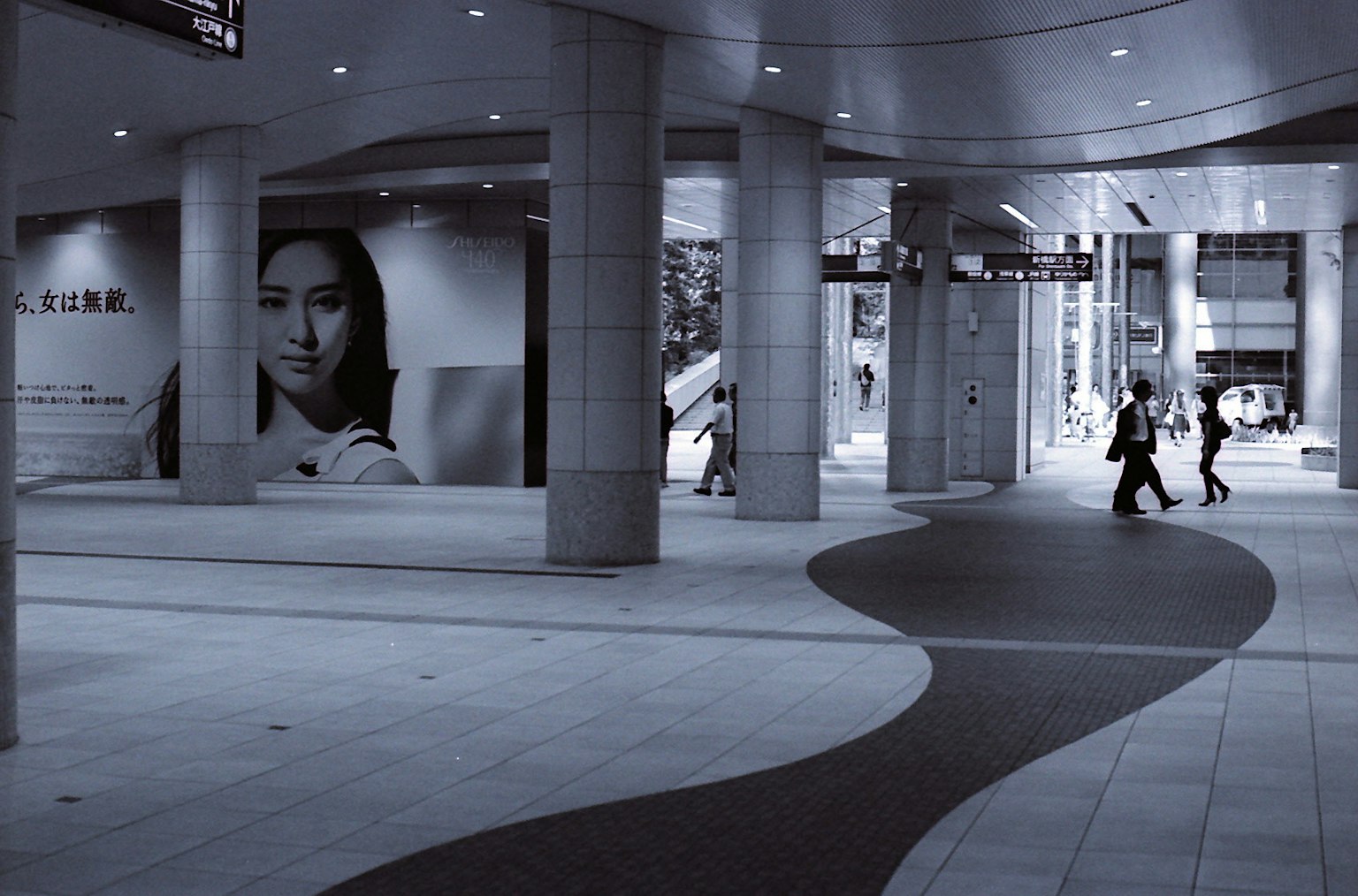 Monochrome urban space with people walking and a large poster of a woman