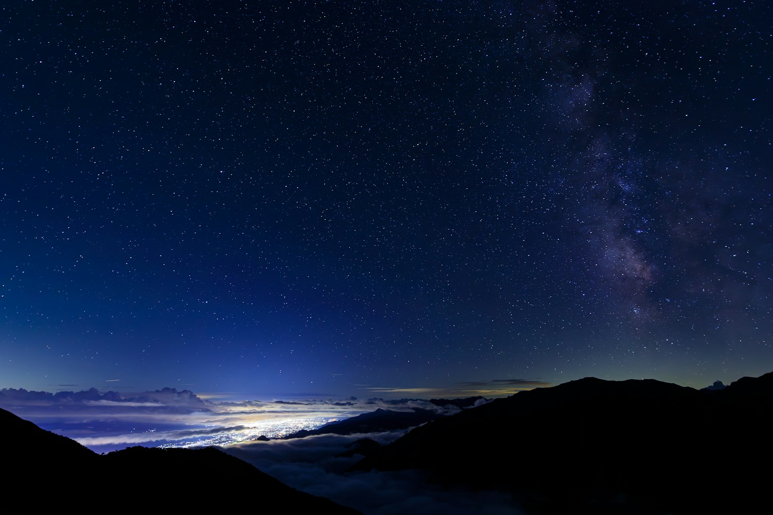 Sternenhimmel über einem Wolkenmeer mit Bergsilhouetten