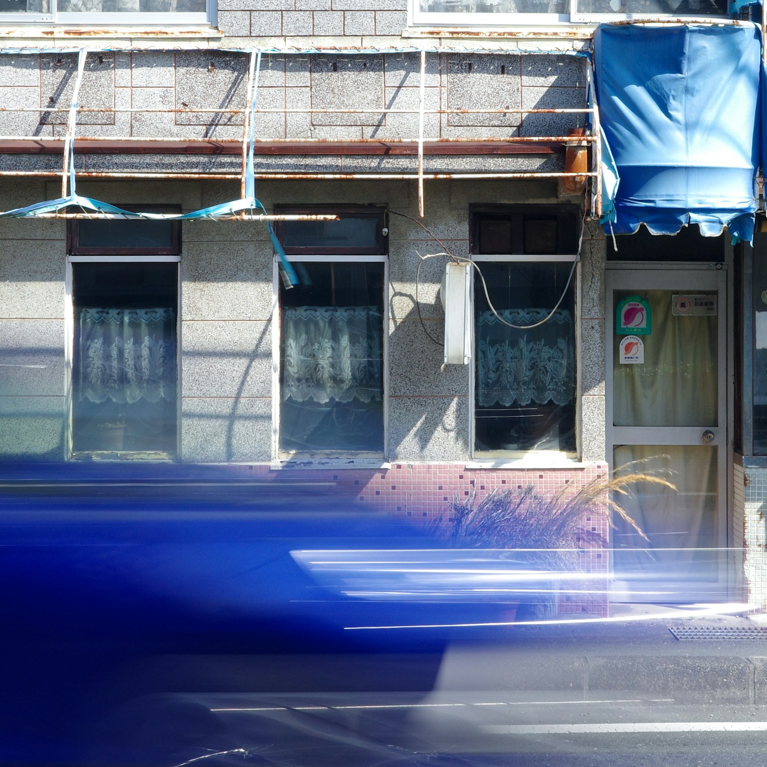 Exterior of an old building with a blue awning and passing car
