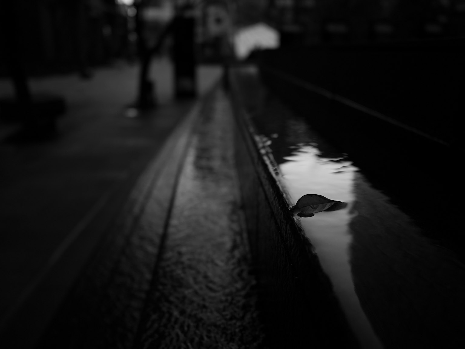 Immagine in bianco e nero di una pozzanghera che riflette la luce e una panchina in legno