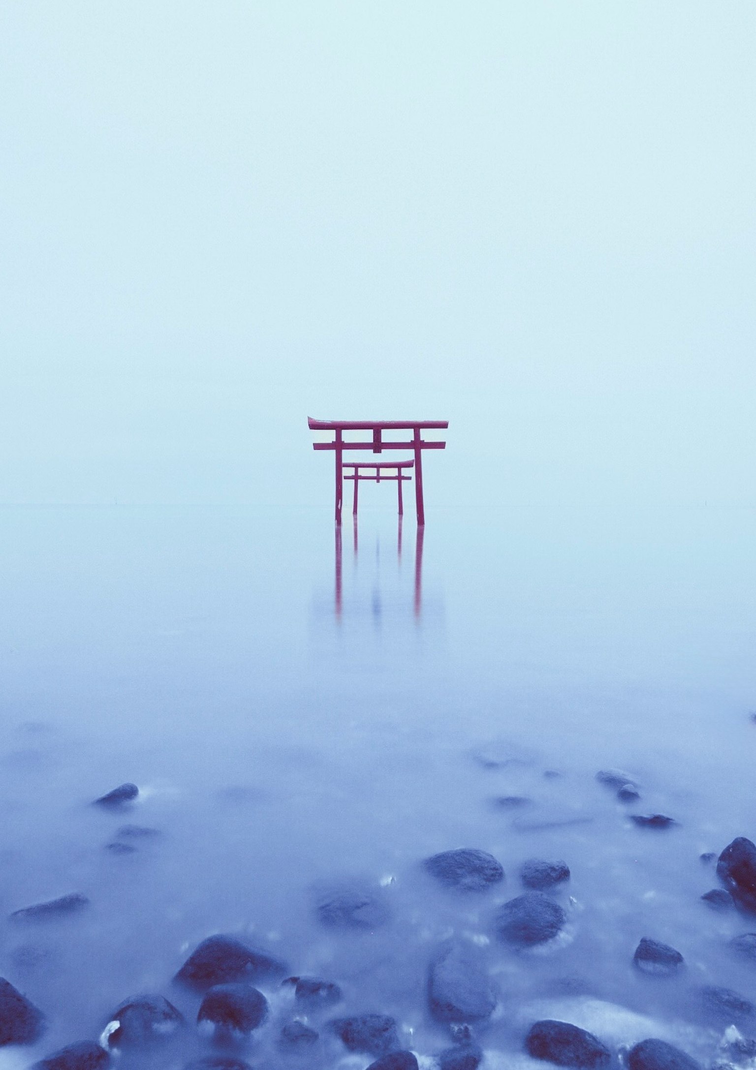 Red torii gate standing in fog over rocky water