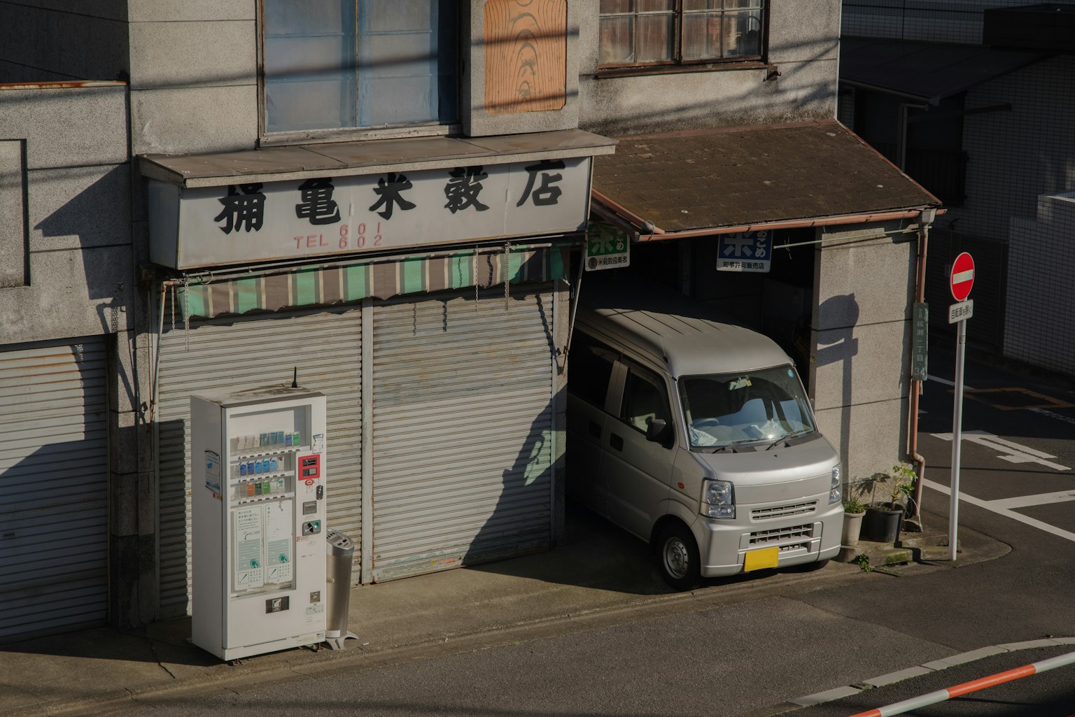 一輛小白廂型車停在舊建築前，旁邊有一台自動販賣機