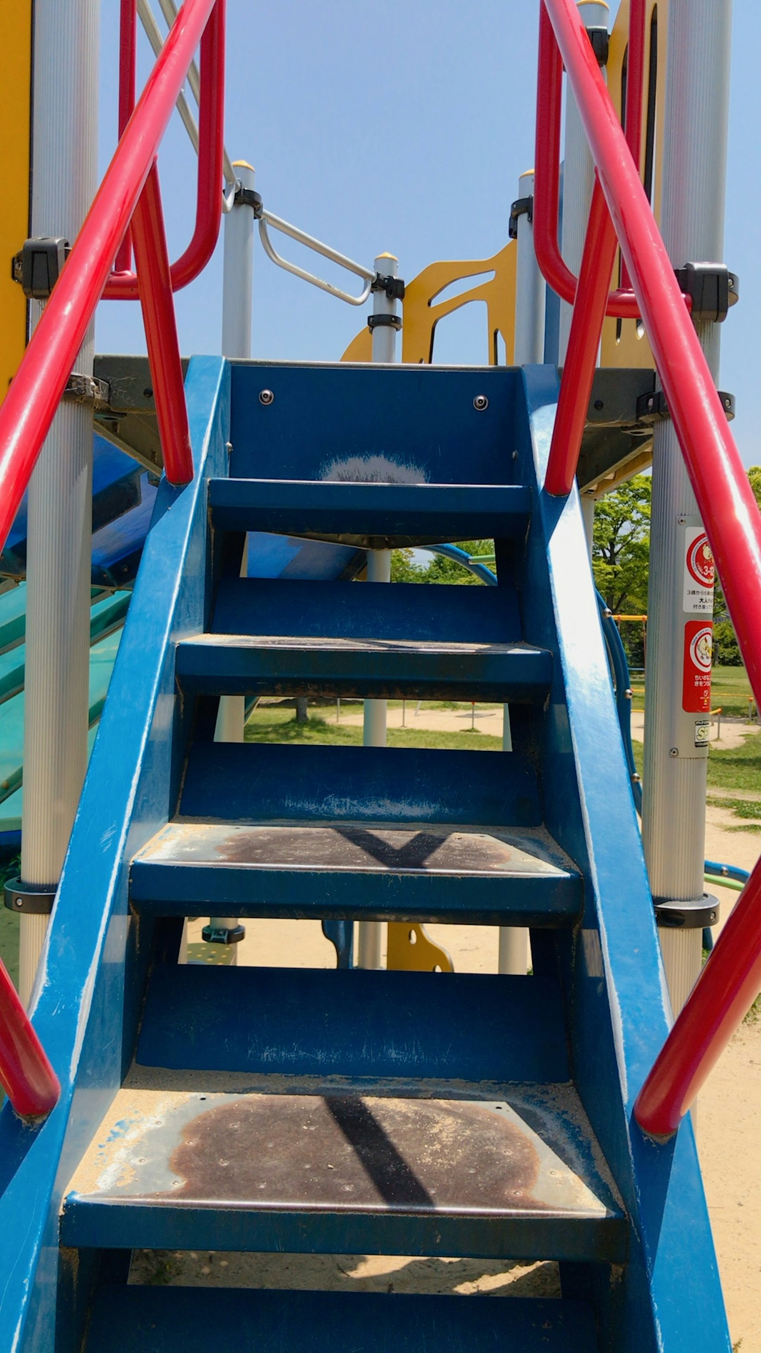 Treppe zu einer blauen Rutsche mit roten Handläufen