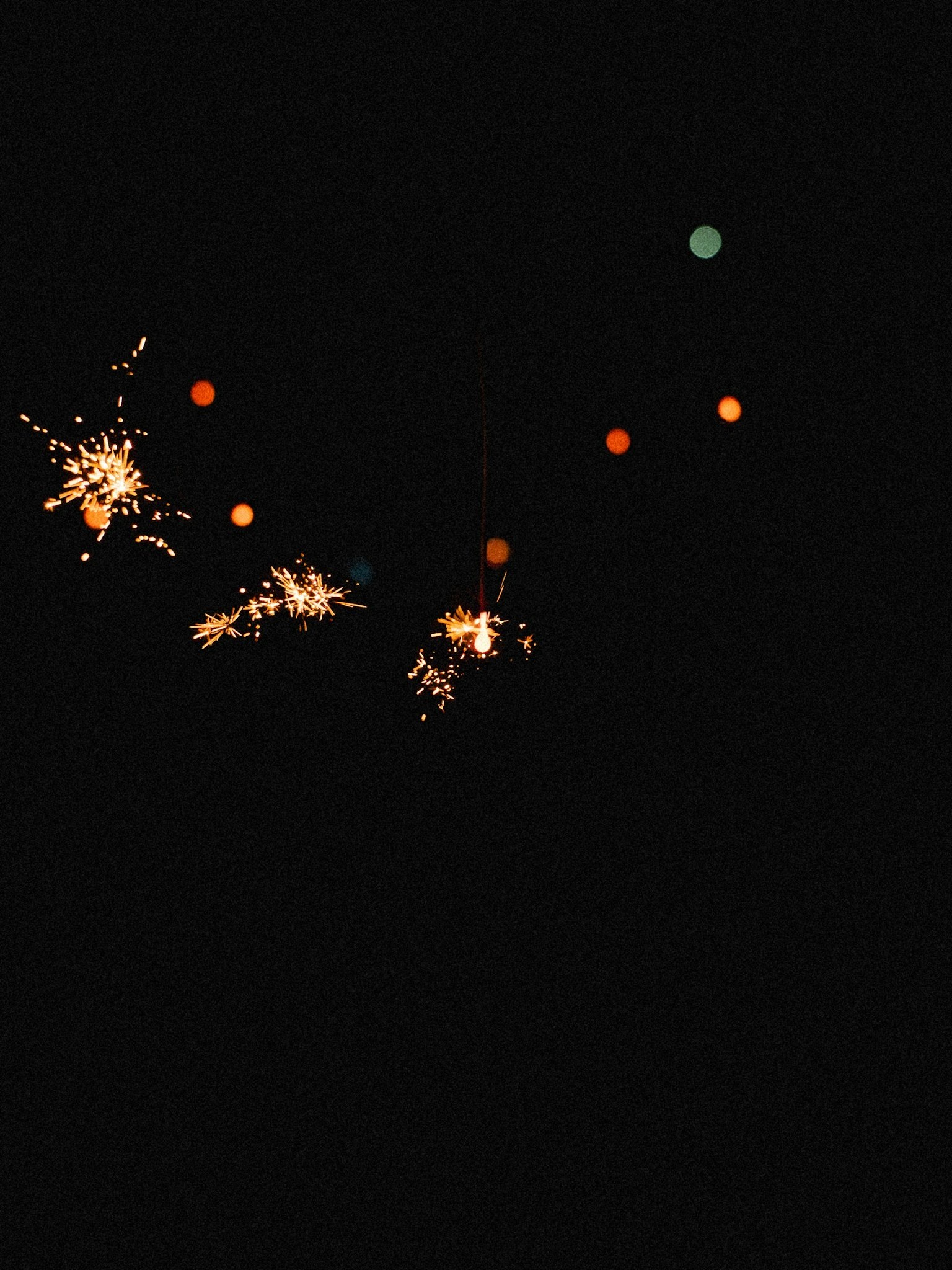Scena notturna con fuochi d'artificio e punti luminosi arancioni su sfondo scuro