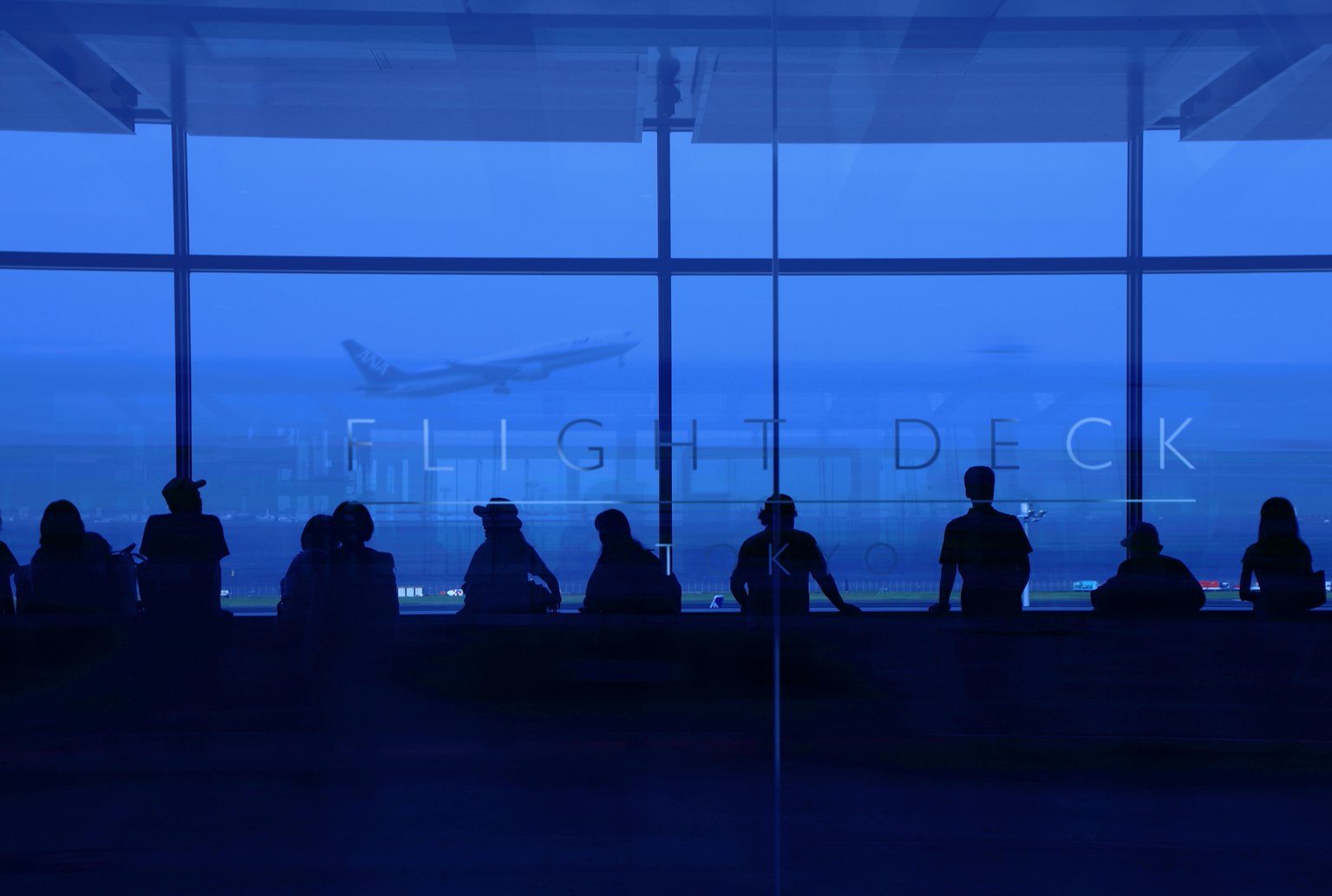 Silhouette orang-orang yang melihat pesawat di bandara yang diterangi biru