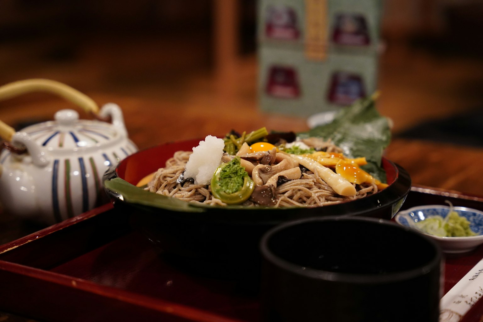 Schön angerichtetes Soba-Gericht mit grüner Garnitur neben einer japanischen Teekanne und einer schwarzen Schüssel