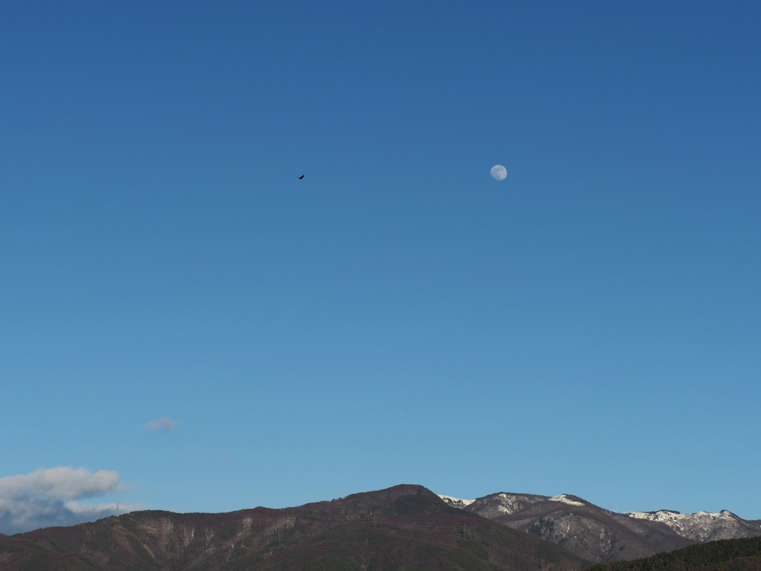 A landscape featuring a bright blue sky and snow-capped mountains with a cloud