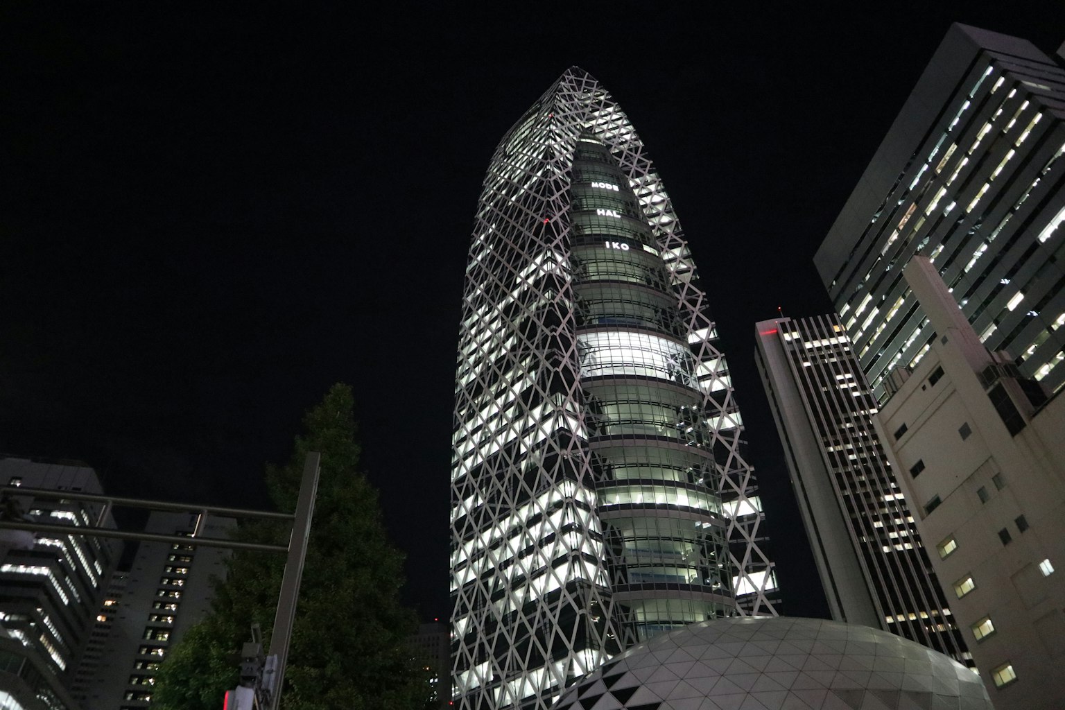 Un rascacielos de diseño único en Shinjuku de noche rodeado de luces de la ciudad