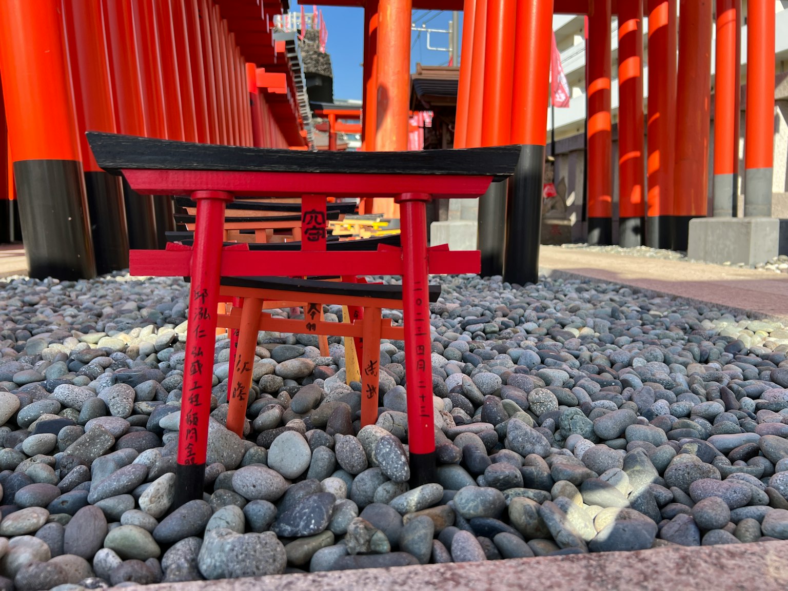 Chiếc ghế đỏ nhỏ trước cổng torii đỏ với nền đá cuội