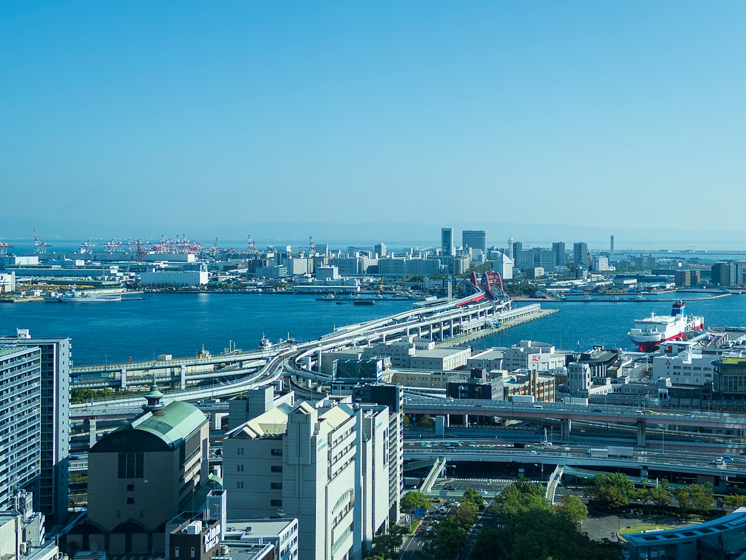 Pemandangan kota dengan pemandangan laut luas menampilkan gedung pencakar langit dan jembatan