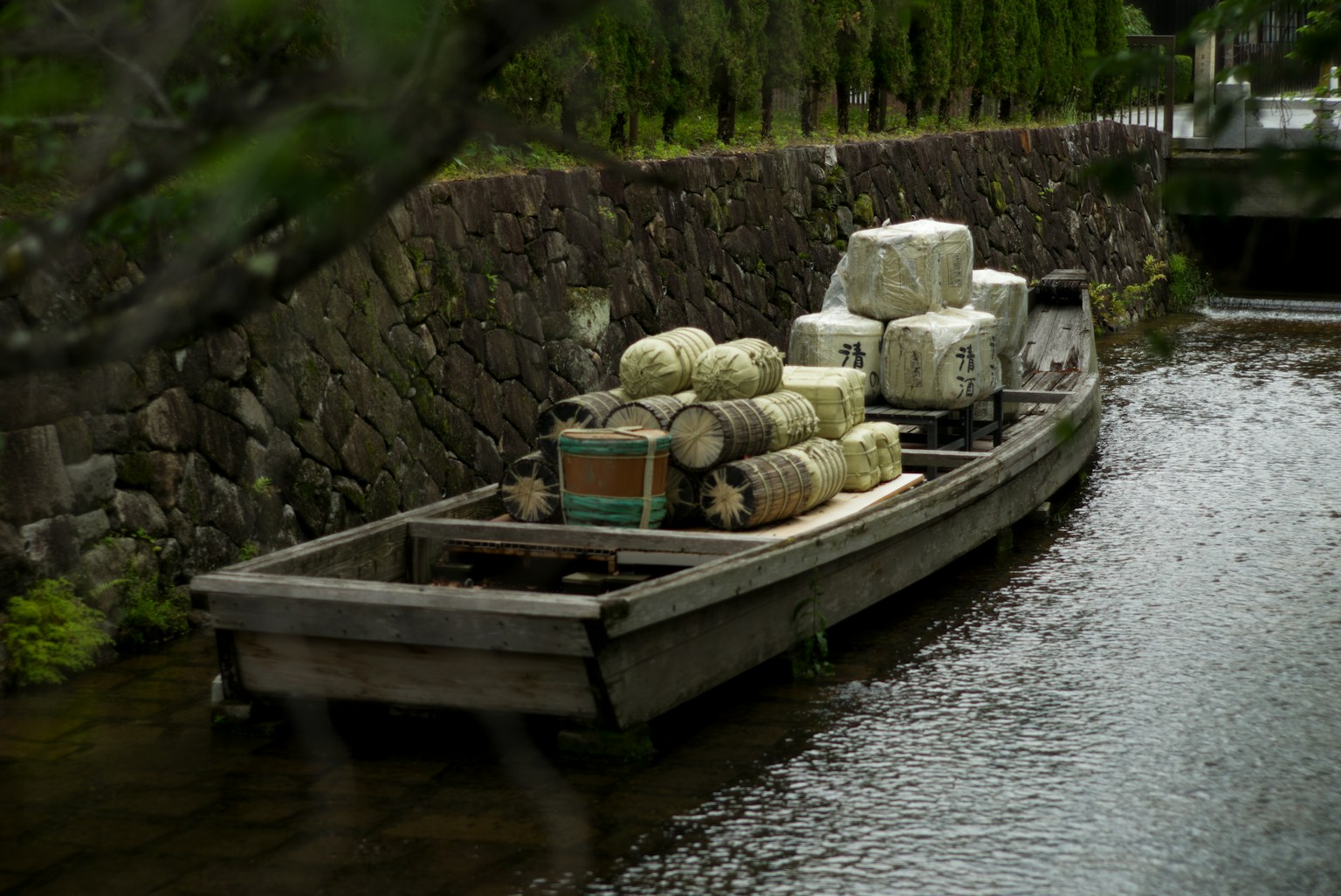 小川に浮かぶ木製の船に積まれた荷物と石垣の風景