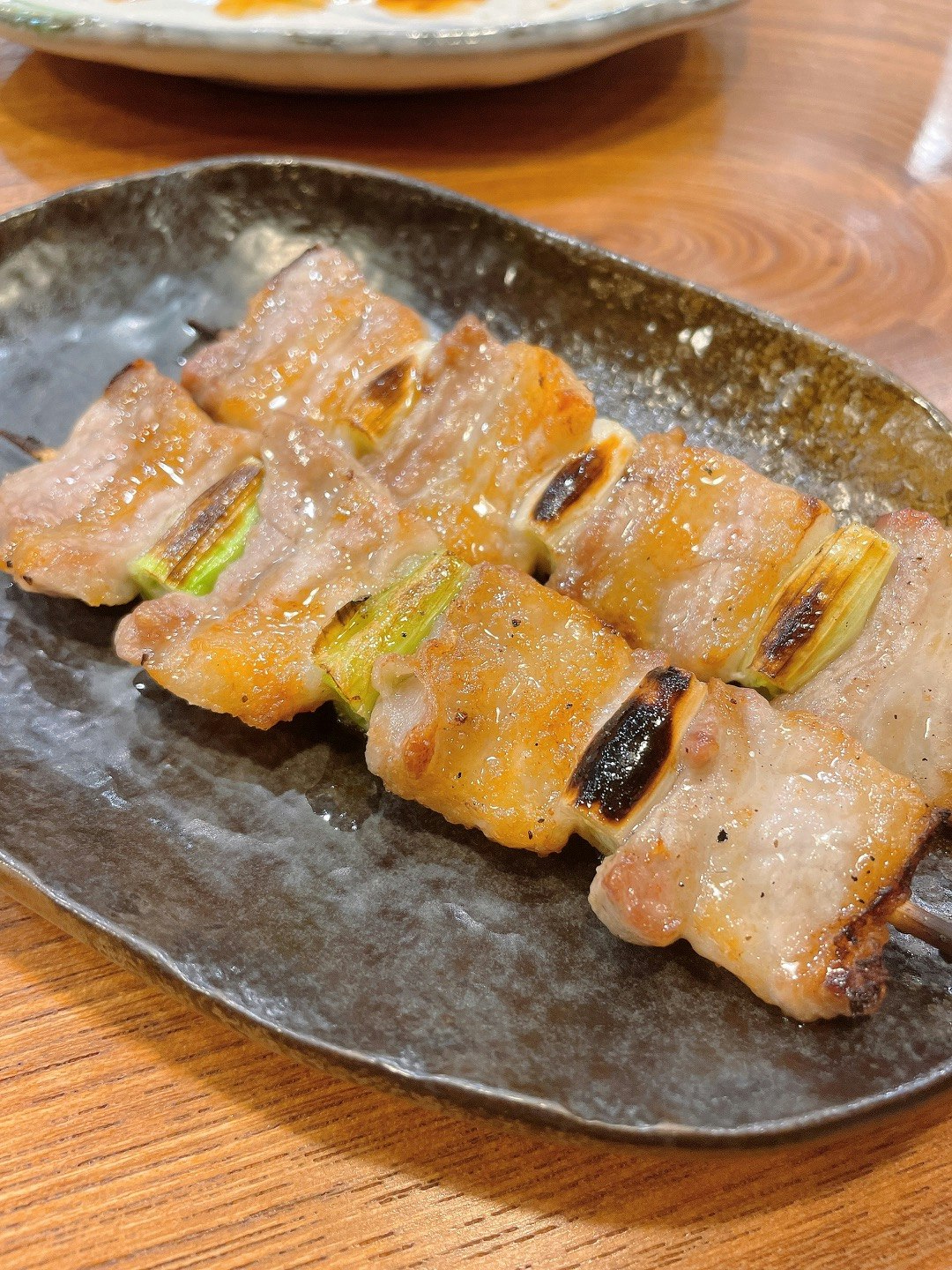 焼き目のついたねぎ入り豚肉の串焼きが皿に盛られた食卓