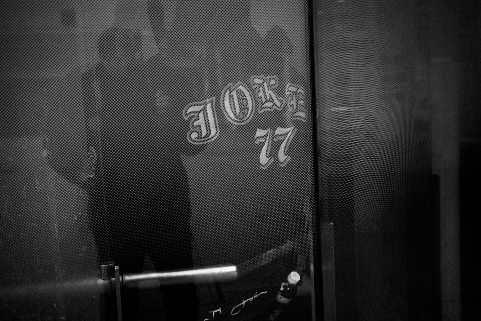 黑色玻璃門上反射的'JOHN 77'文字