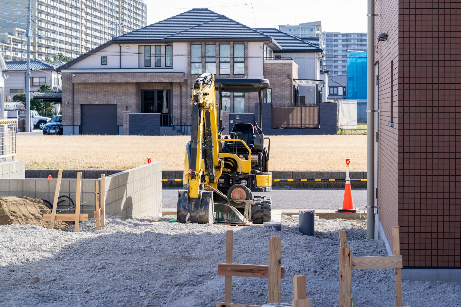 Cantiere di costruzione con un piccolo escavatore e edifici residenziali sullo sfondo