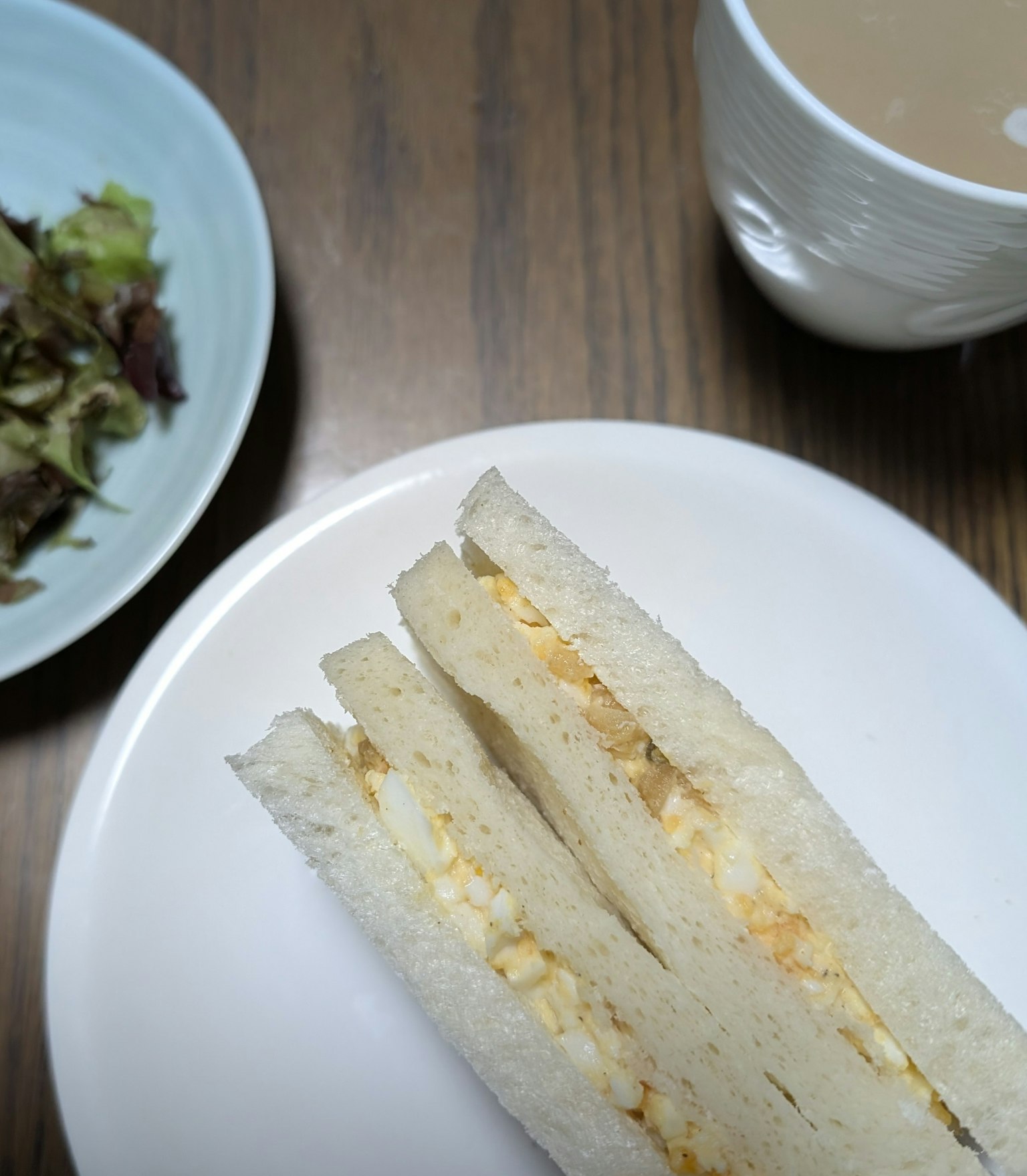 Une assiette de sandwich aux œufs avec un bol de salade et une tasse de café sur une table en bois