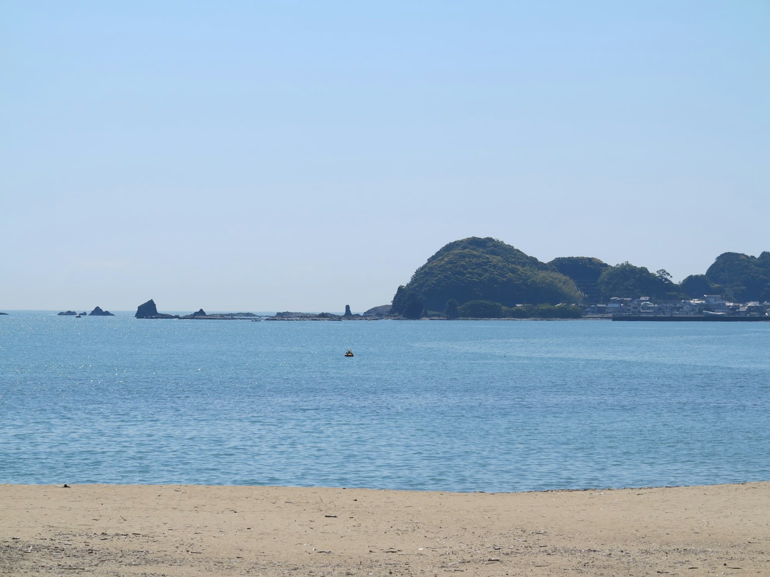 ทิวทัศน์ที่สวยงามของทะเลสีน้ำเงินและชายหาดทราย มีภูเขาและเมืองอยู่เบื้องหลัง