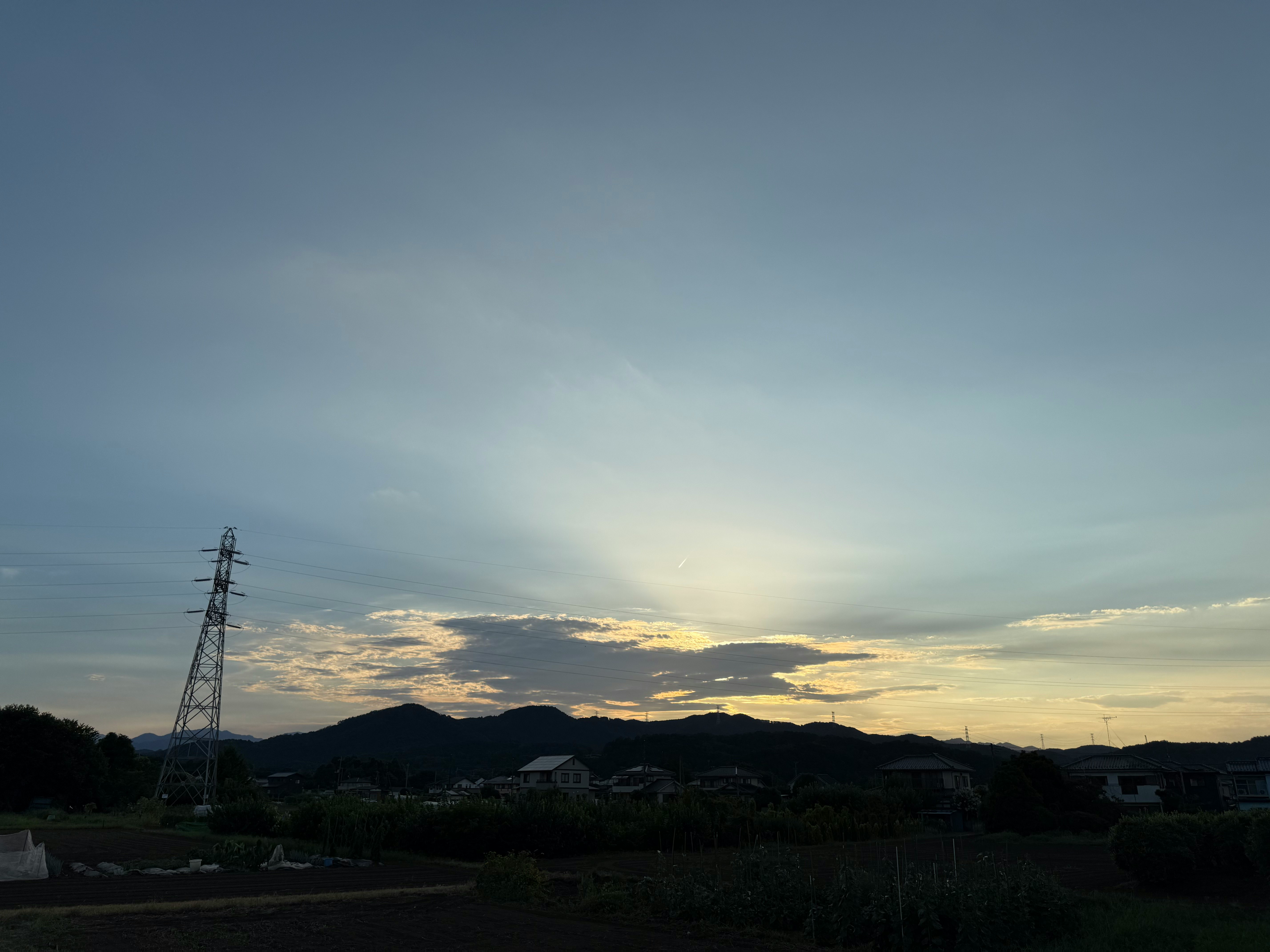 夕暮れの田園風景と遠くの山並み、送電鉄塔のある空