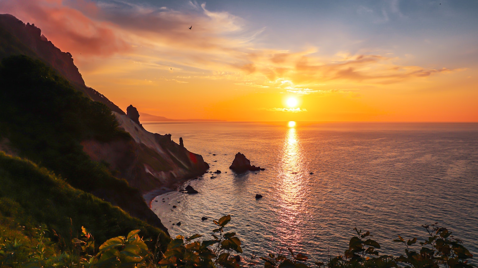 Paysage magnifique du coucher de soleil sur l'océan avec des rochers et des collines vertes