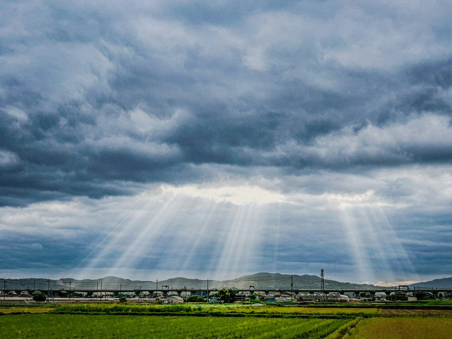 陽光透過陰雲灑在綠色鄉村風景上