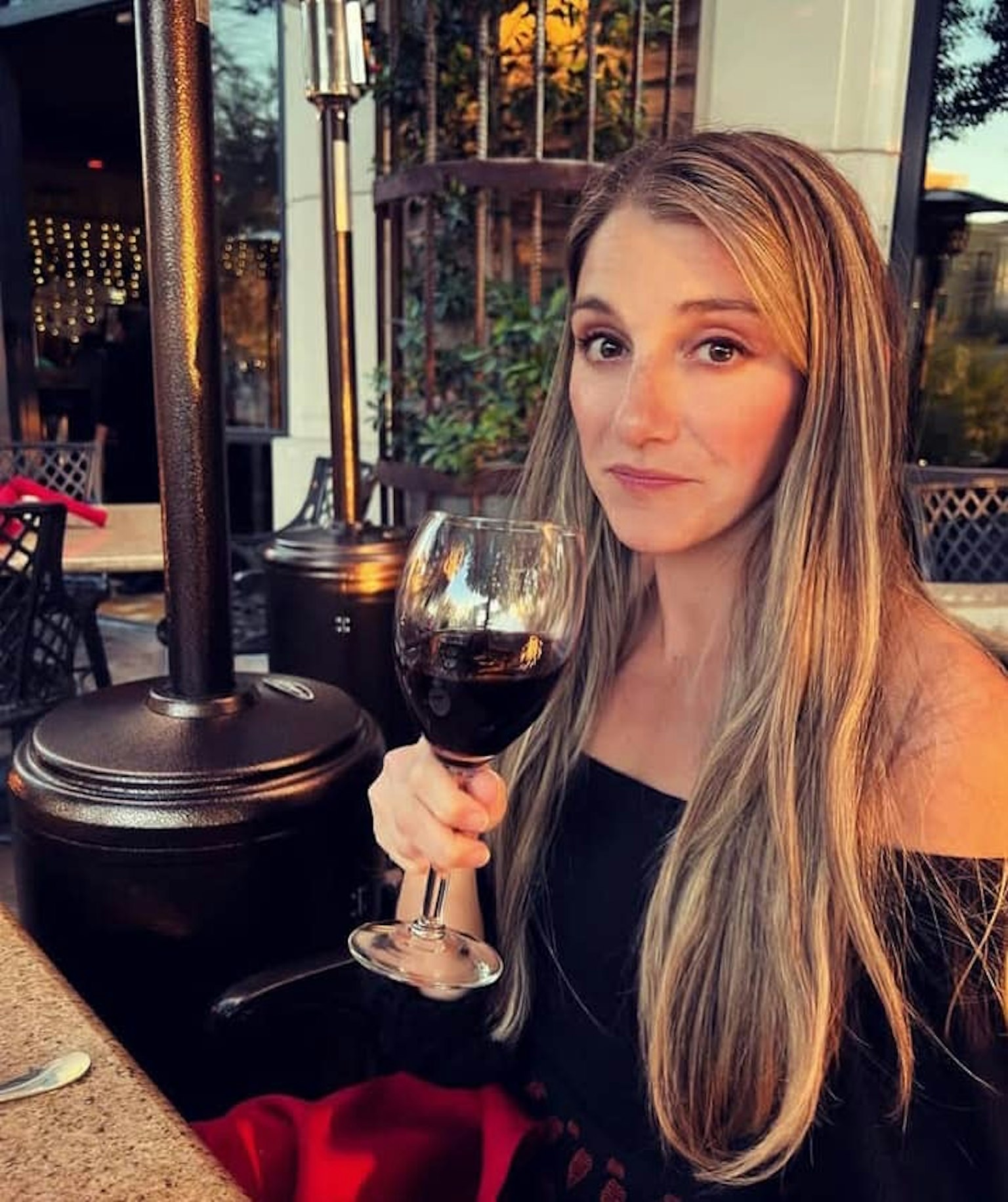 女性が赤ワインを持って微笑んでいる屋外のレストランのシーン