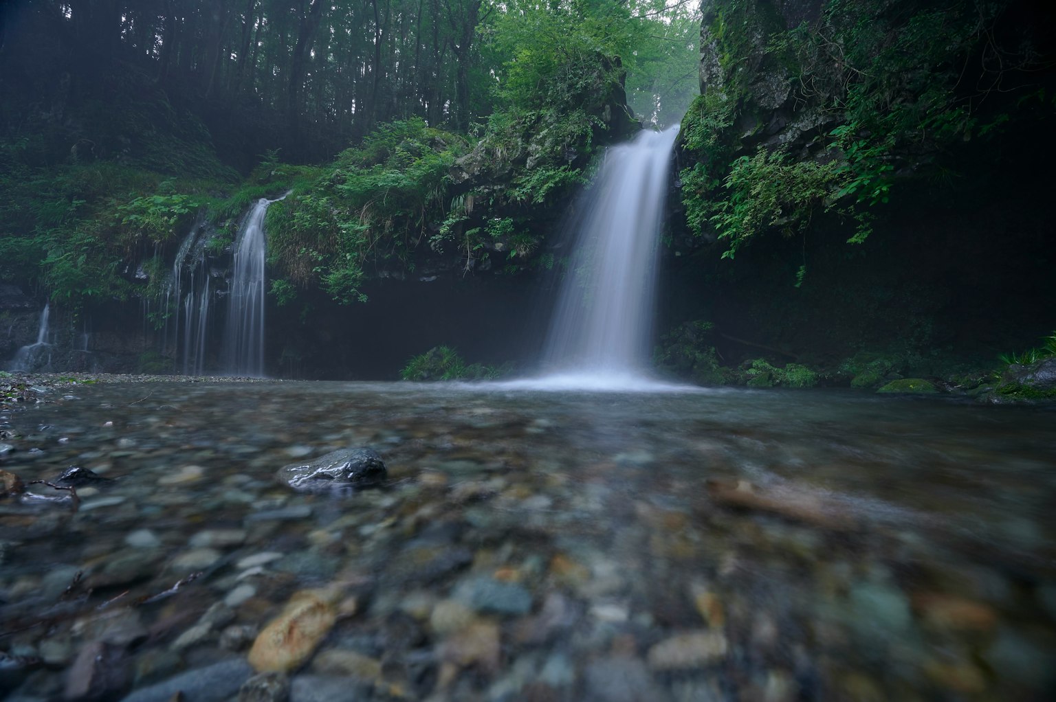Serene waterfall cascading into a clear stream surrounded by lush greenery