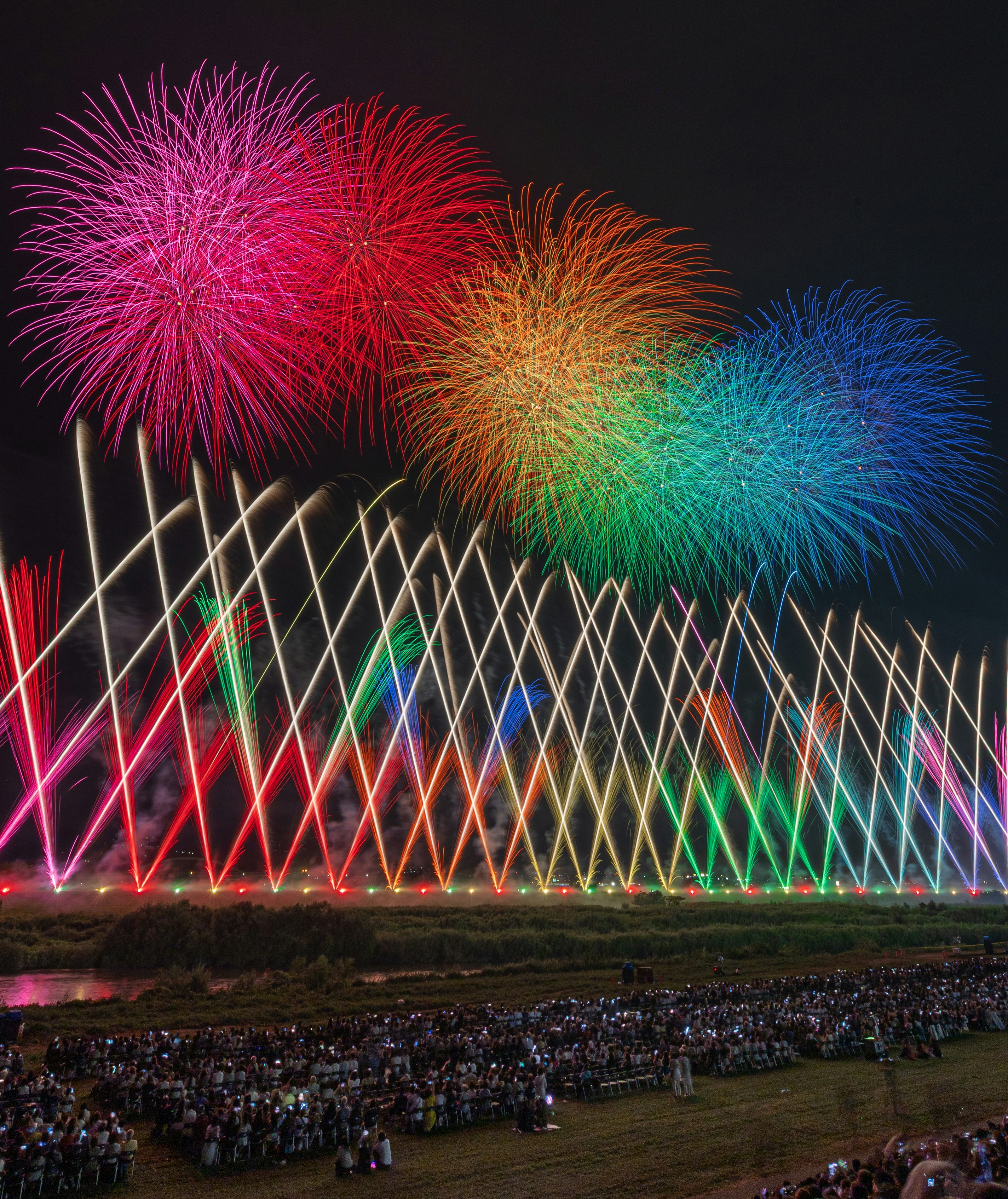 夜空に咲くカラフルな花火と観客の群れ