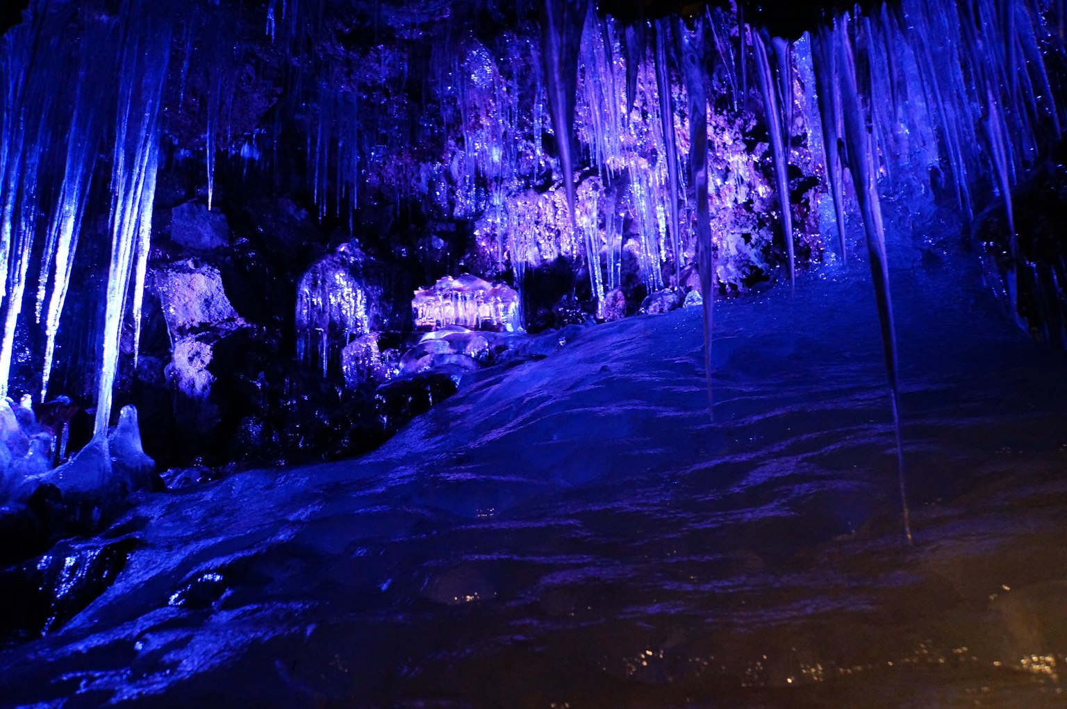 Intérieur de la grotte avec des stalactites de glace suspendues éclairées par une lumière bleue