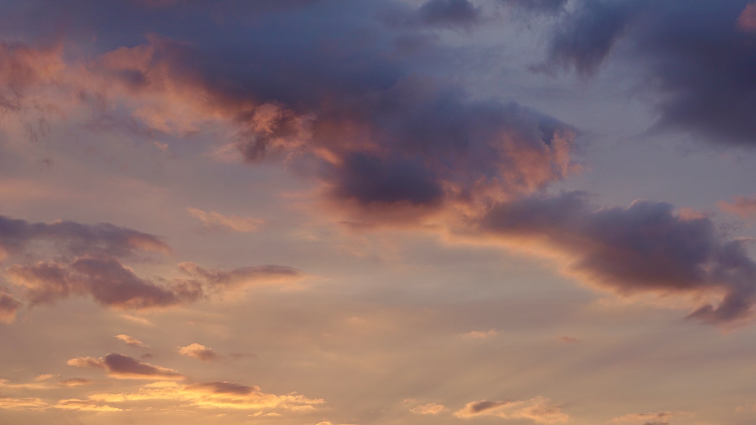 Wolken in Lila- und Orangetönen vor einem Sonnenuntergangshimmel