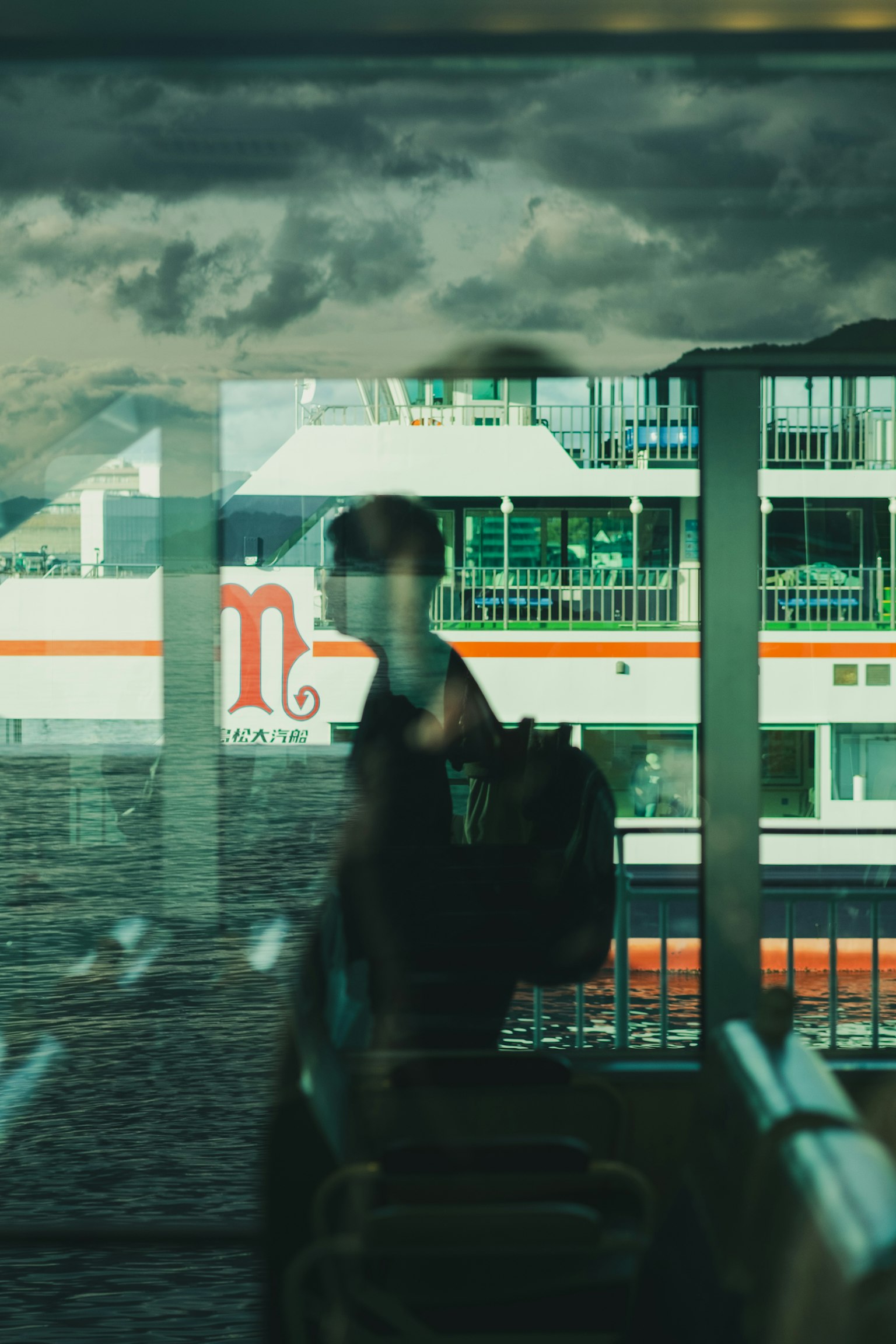 Silhouette einer Person mit einem Rucksack, gesehen durch ein Fenster, das Wasser und ein Boot reflektiert