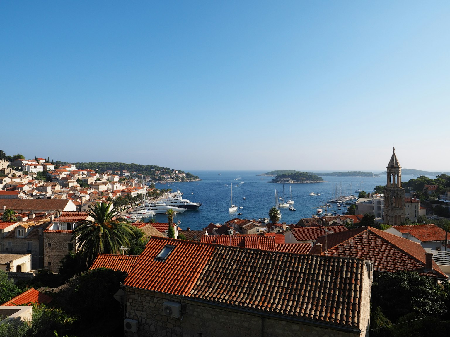 Scenic view of a coastal town with red rooftops and sailboats on the blue sea