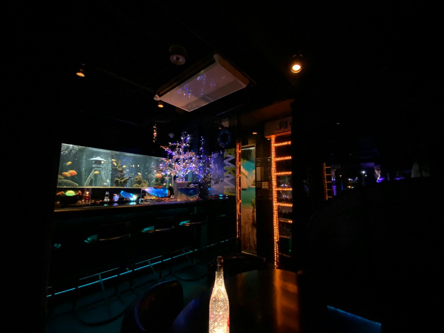 Escena interior de un bar con un acuario en un ambiente oscuro