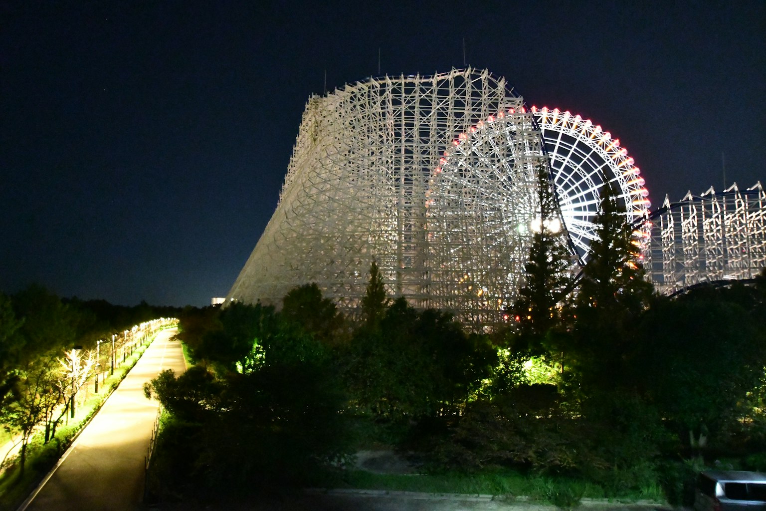 Pemandangan malam roller coaster kayu dan bianglala di taman hiburan