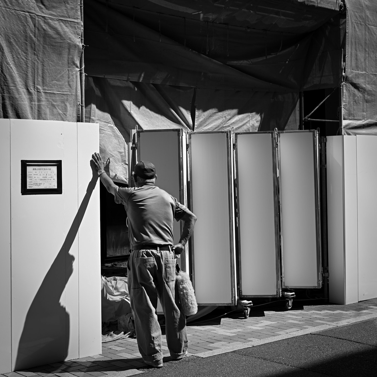 A man leaning against a white panel deep in thought in a black and white image