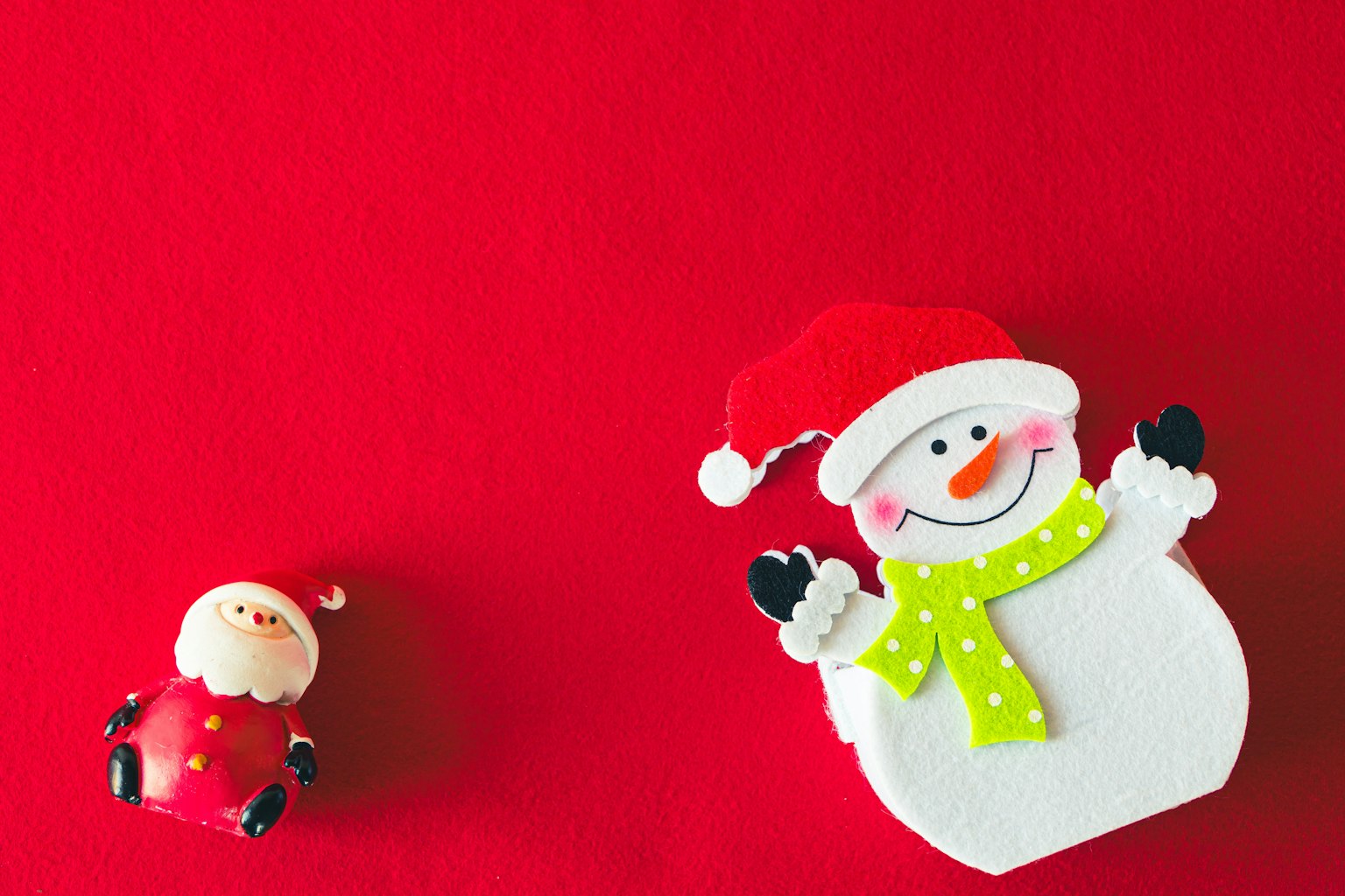 Seorang manusia salju mengenakan topi Santa dan Santa kecil berpakaian merah di latar belakang merah