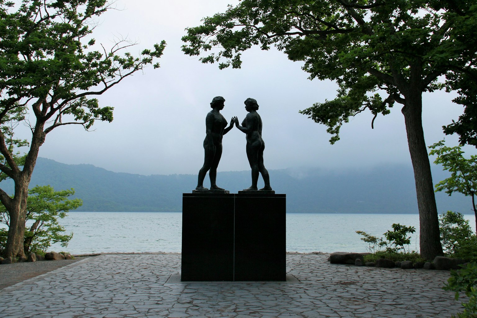 Dos figuras frente a frente frente a un lago