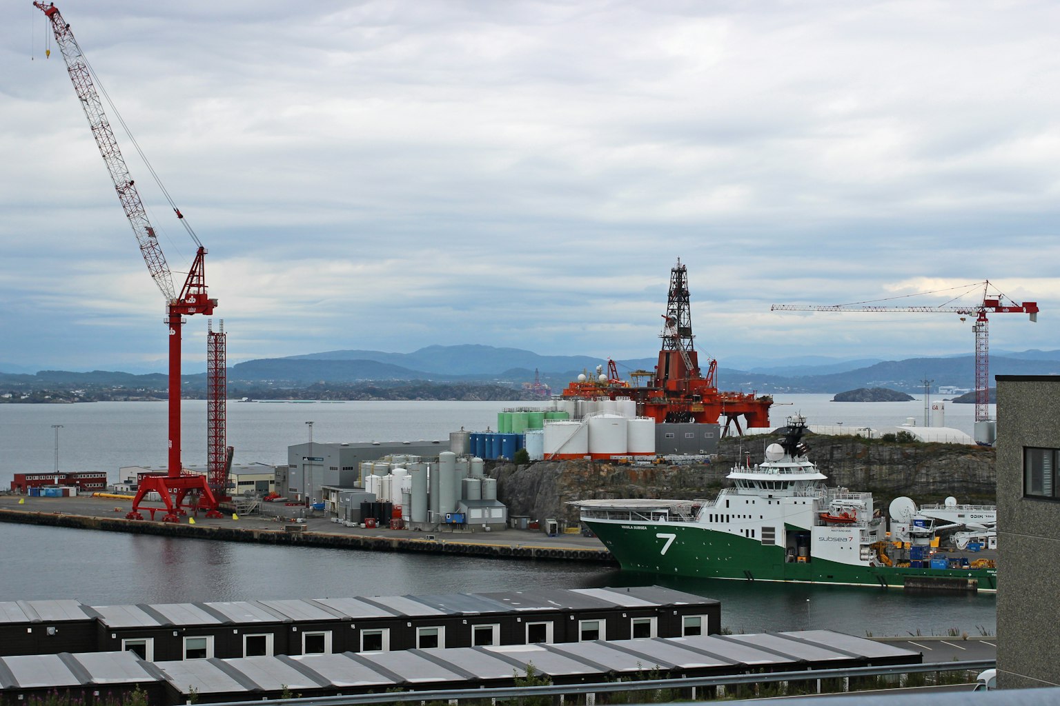 Zone industrielle avec un bateau vert amarré et des grues au port