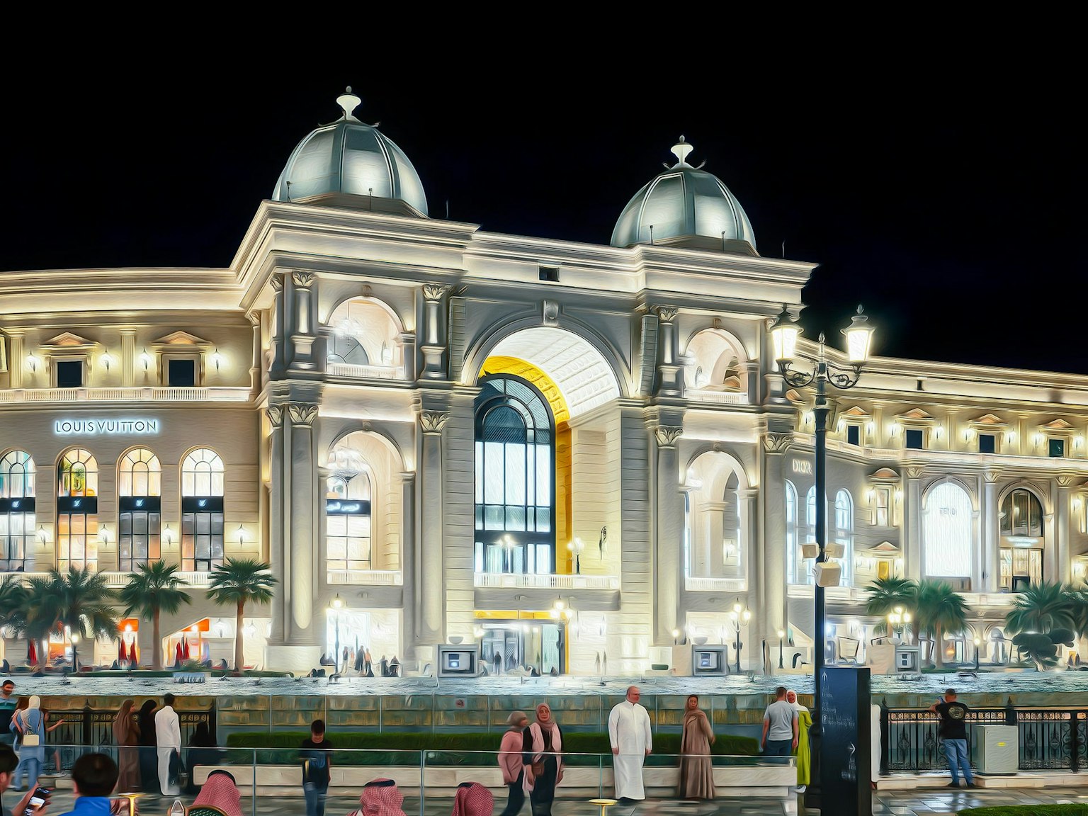 Hermosa fachada de edificio por la noche con luces brillantes y techos en cúpula gran entrada en arco y palmeras circundantes