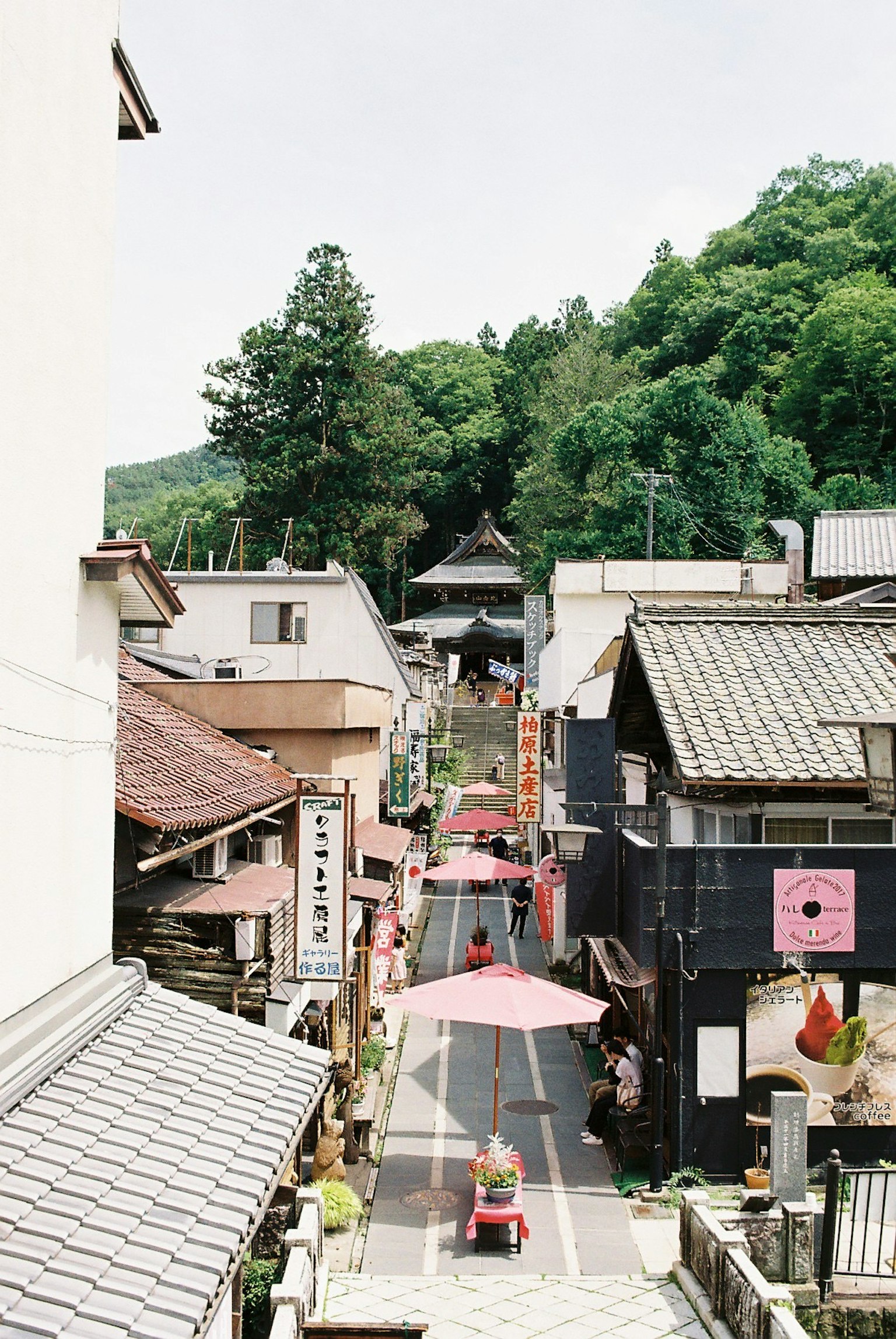 Scenic view of a street lined with traditional buildings and pink umbrellas under a mountain
