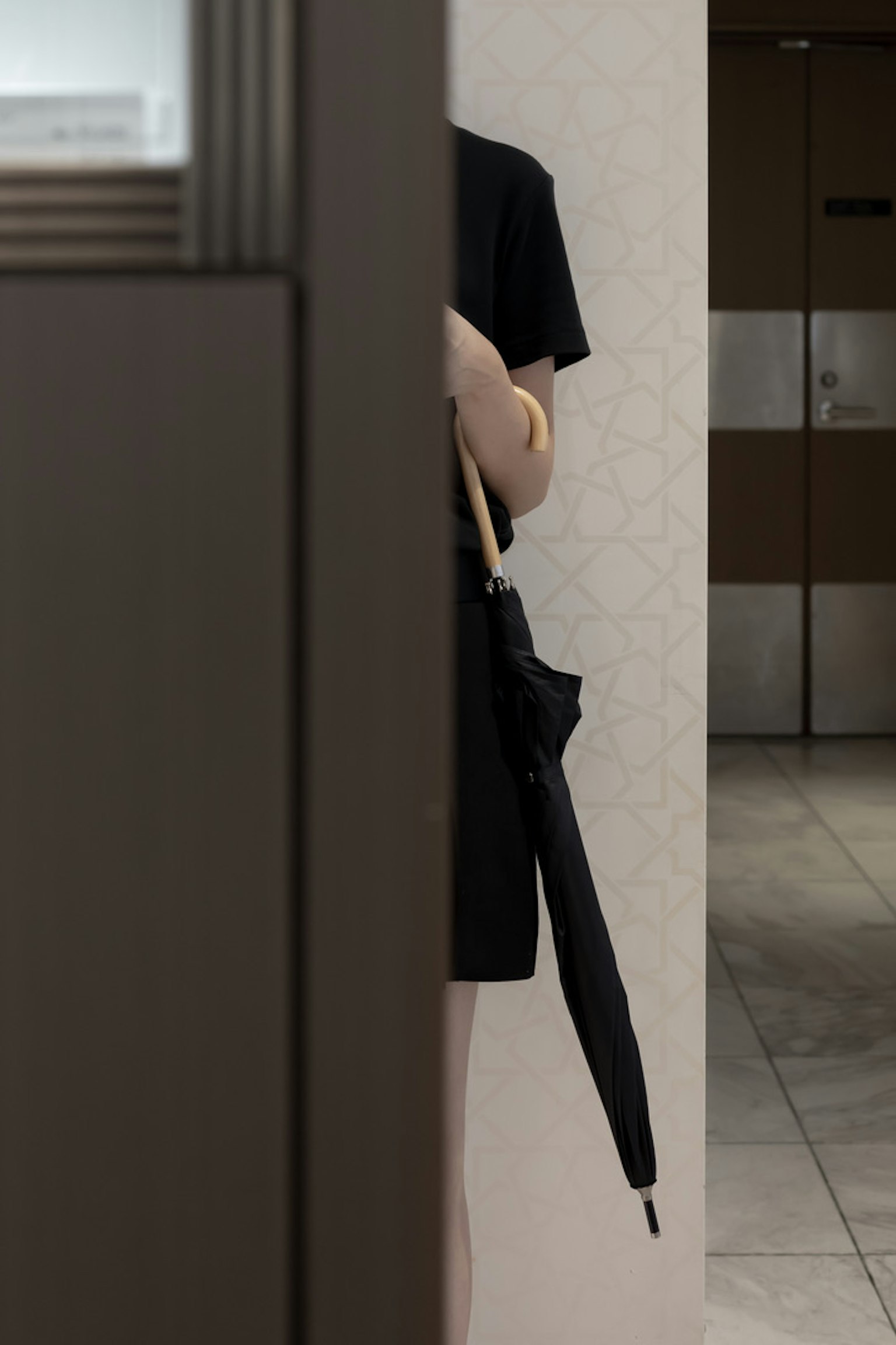 A person in black clothing holding an umbrella partially obscured by a wall